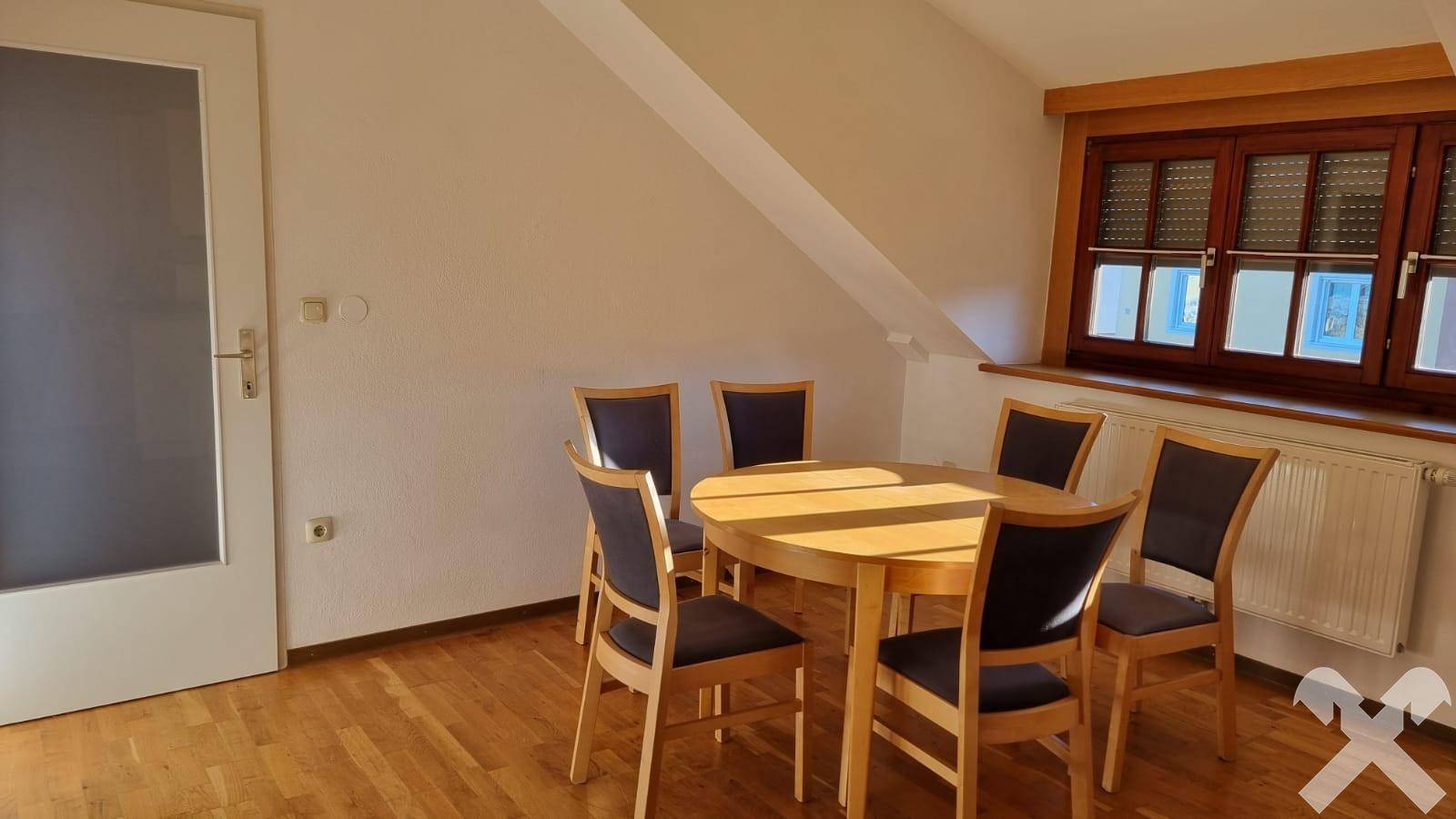 Gemütlicher Essbereich mit Holztisch und Stühlen unter einer Dachschräge.