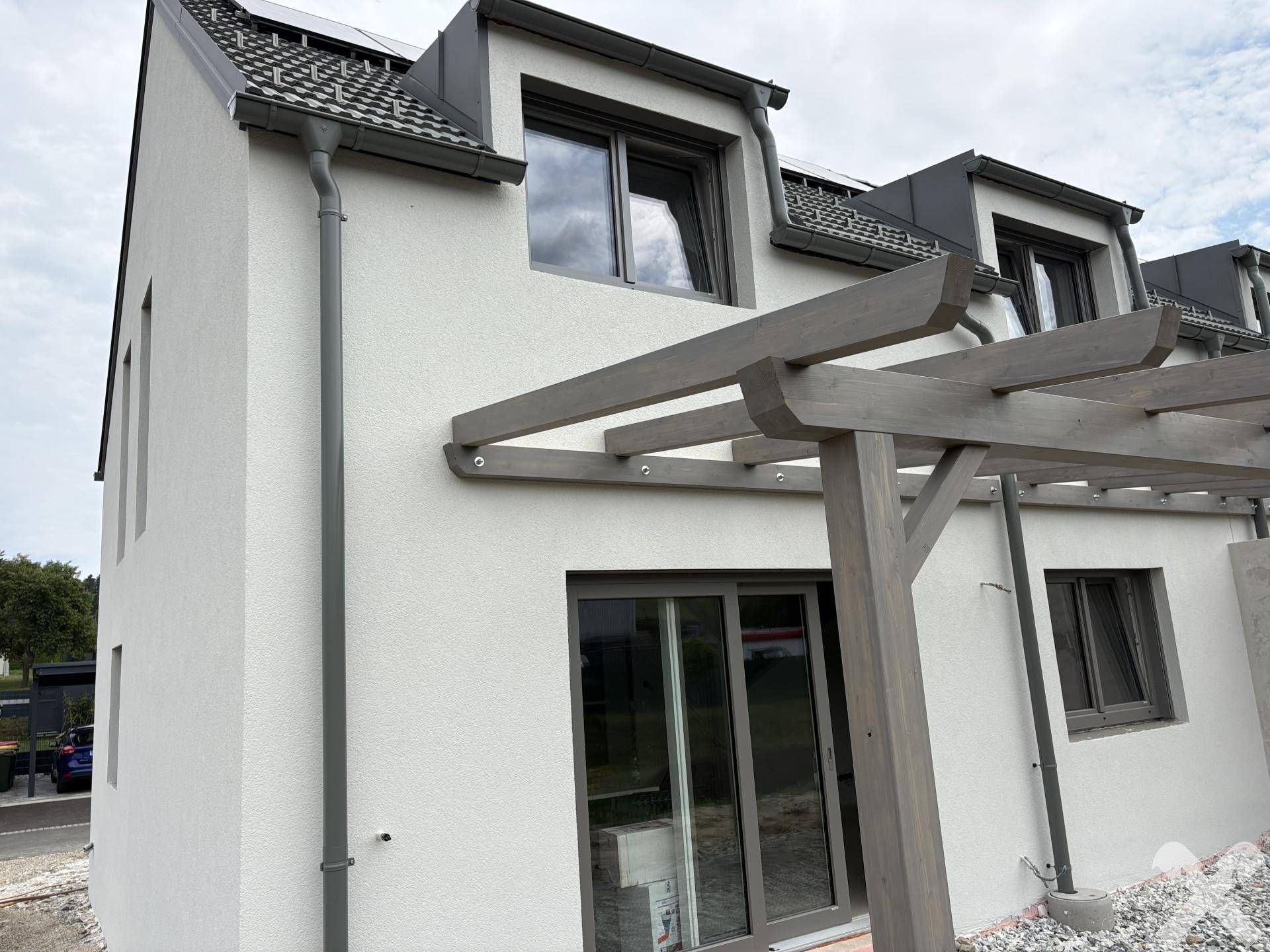 Seitenansicht einer Neubau-Doppelhaushälfte mit Pergola-Struktur und modernen Fenstern.