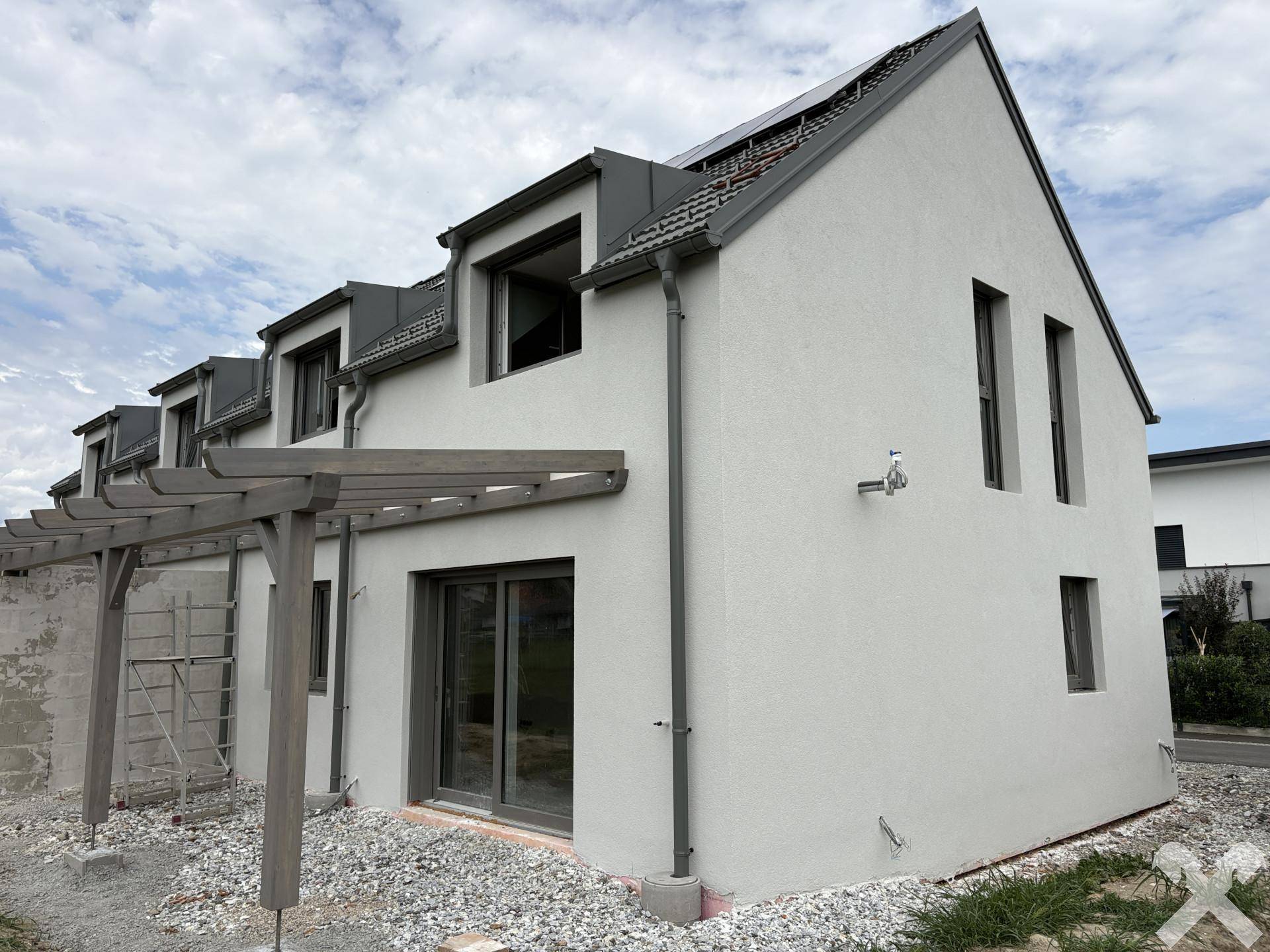 Schräge Ansicht der Neubau-Reihenhäuser mit weißer Fassade und grauen Dächern unter bewölktem Himmel.