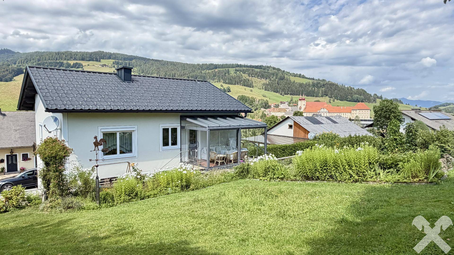 Gartenbereich mit Wintergarten und weitem Blick auf die umliegende Landschaft und ein Kloster.