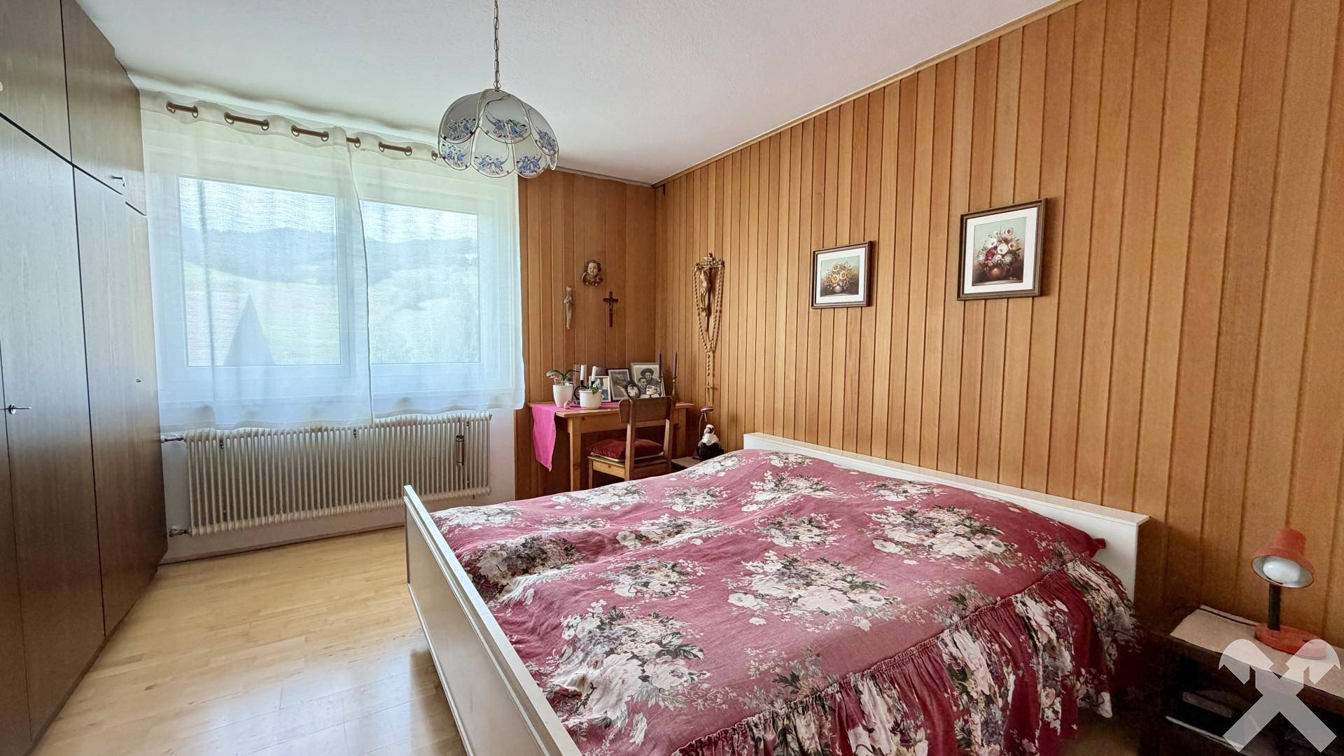 Schlafzimmer mit Holzvertäfelung, Doppelbett und Blick auf die grüne Umgebung.