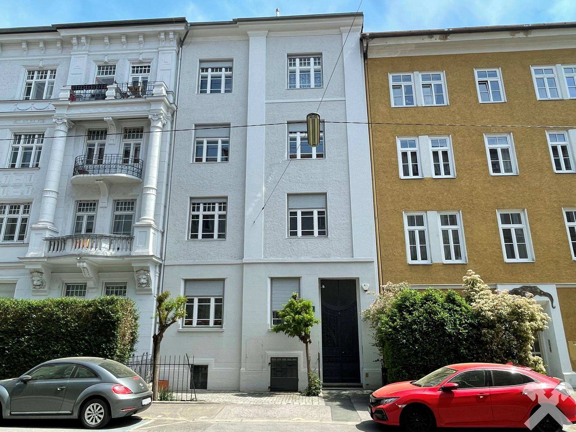Fassade eines Mehrfamilienhauses mit klassischer Architektur und angrenzenden Gebäuden an einer Straße.
