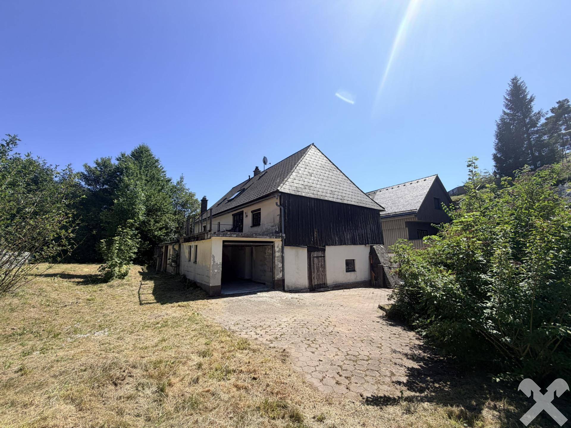 Rückansicht des Hauses mit Garage, trockenem Rasen und Bergblick an einem sonnigen Tag.