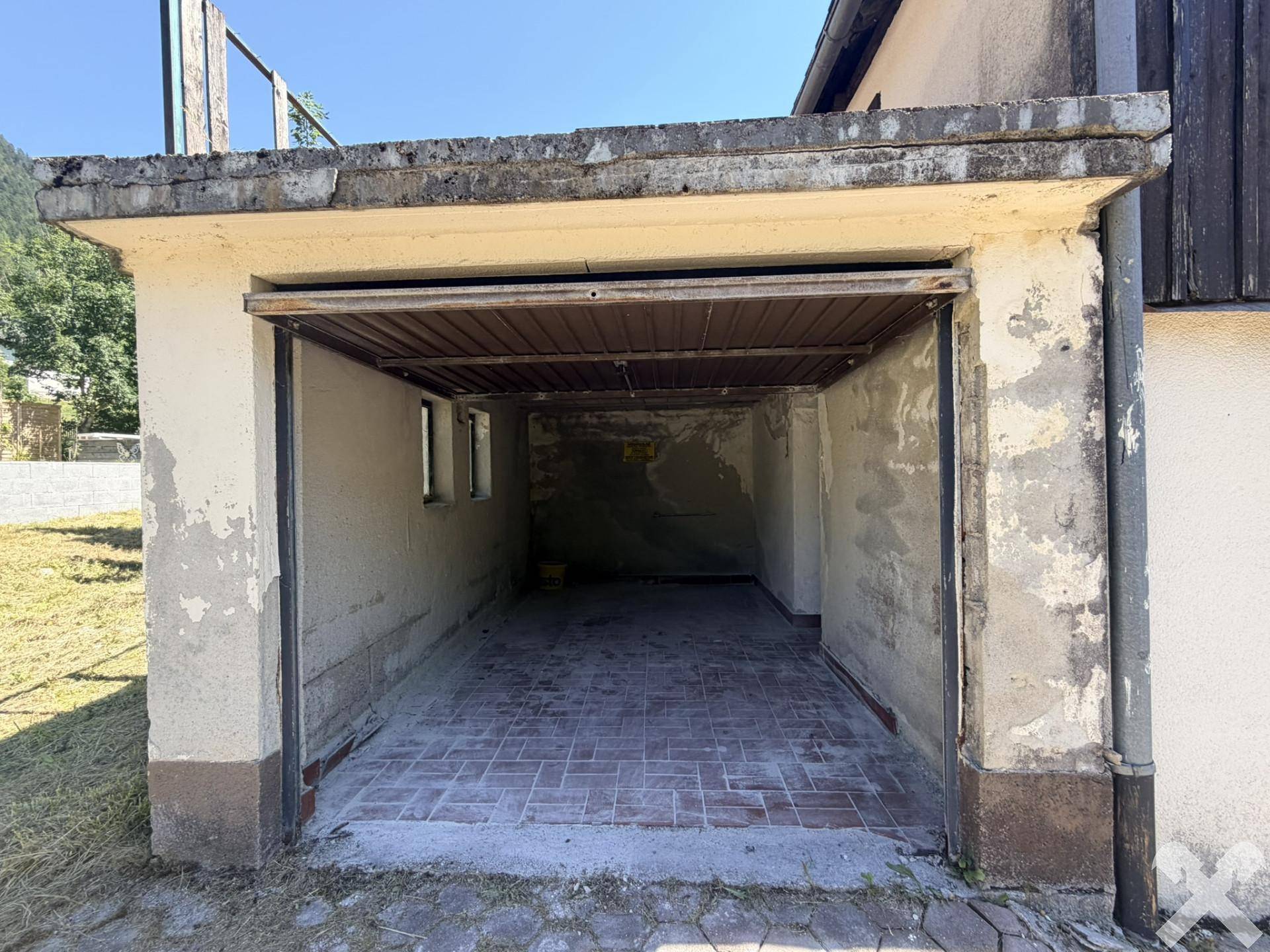 Leere Garage mit Ziegelboden und Rolltor, bereit zur Nutzung.