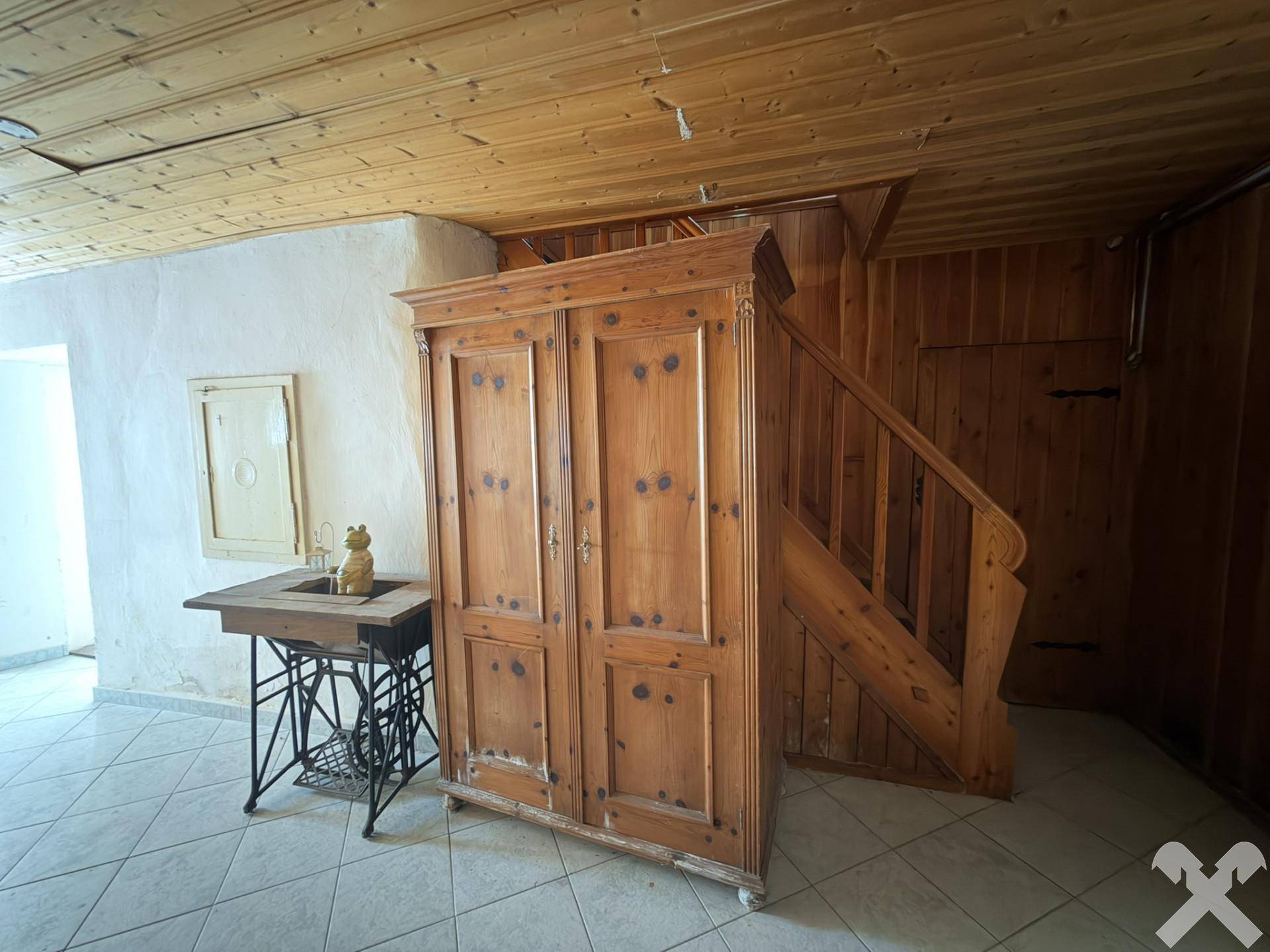Eingangsbereich mit Fliesenboden, Holzschrank und traditioneller Holztreppe.