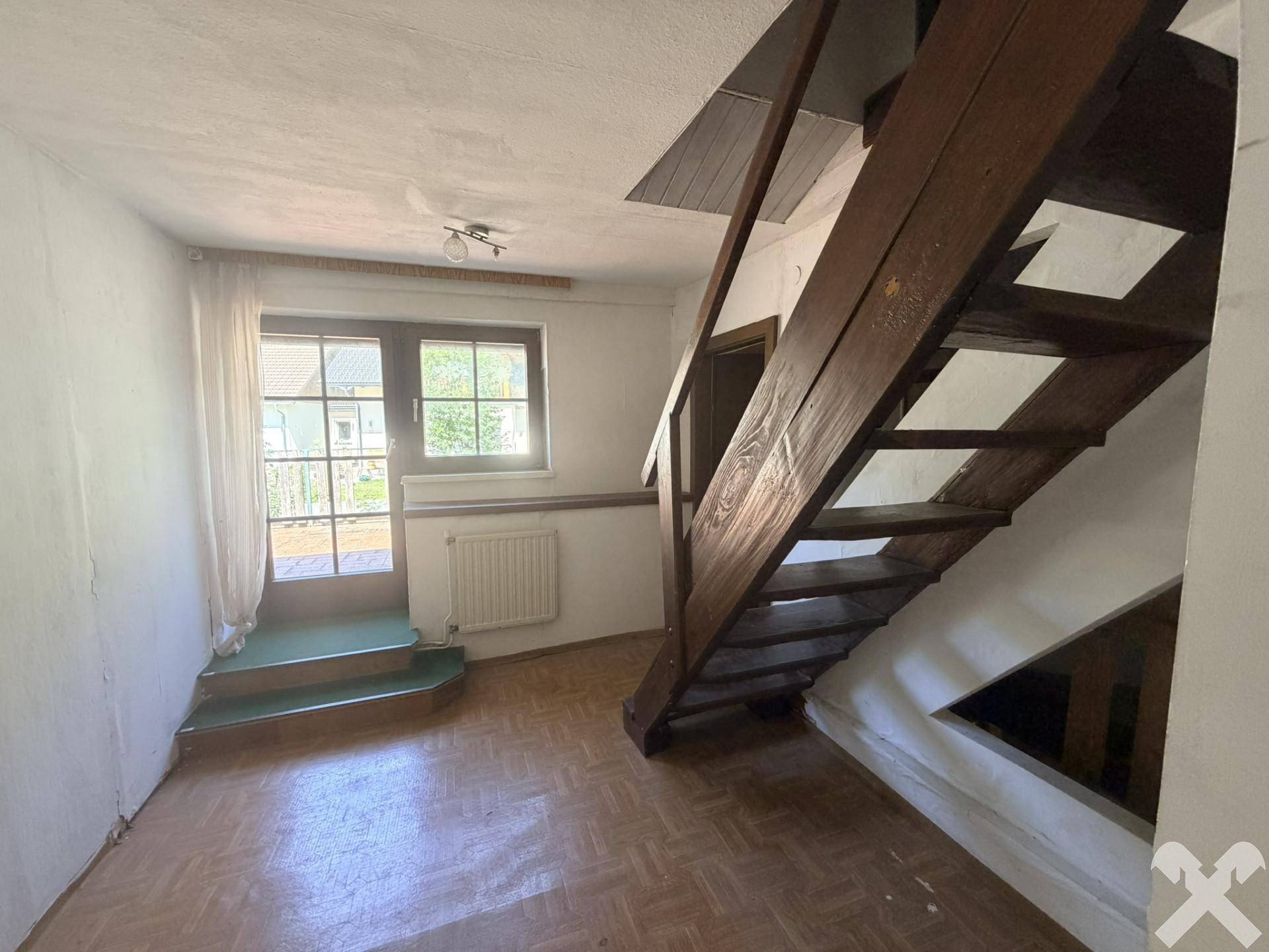 Heller Raum mit Parkettboden, Holztreppe und Zugang zum Außenbereich.