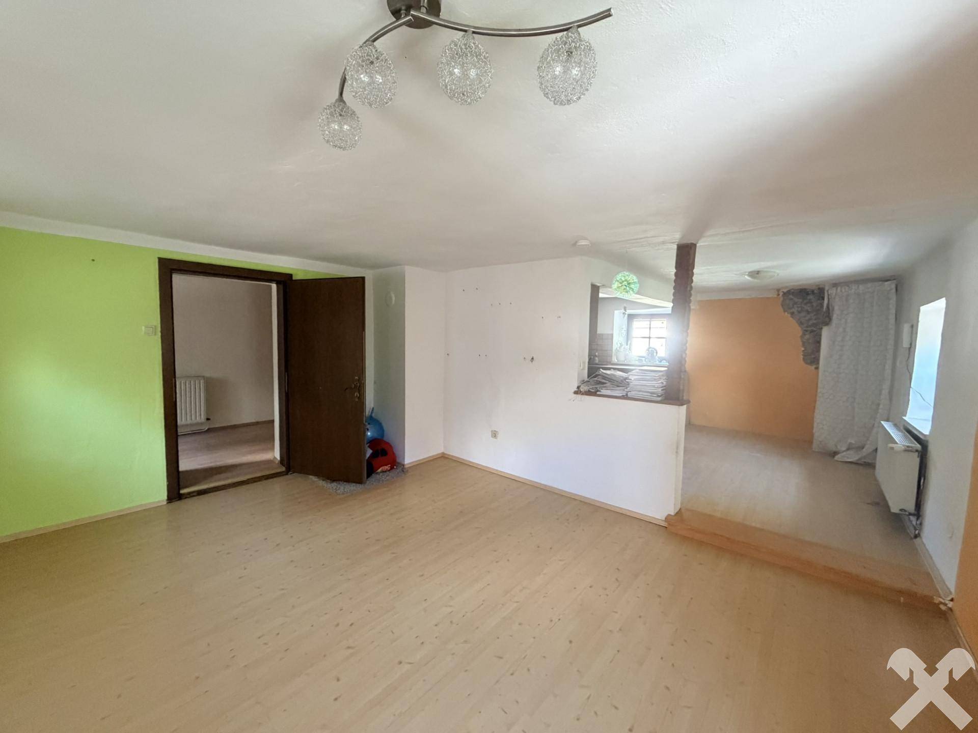 Helles Wohnzimmer mit Laminatboden, grünen Wänden und offenem Übergang zu einem weiteren Bereich.
