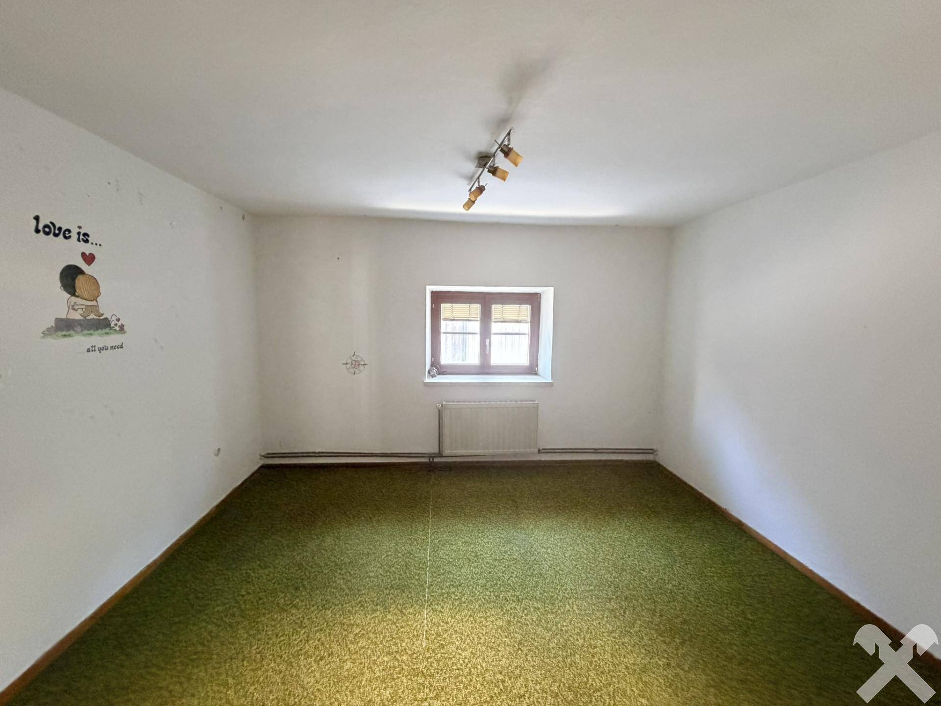 Leeres Zimmer mit grünem Teppichboden, weißen Wänden und einem Fenster.