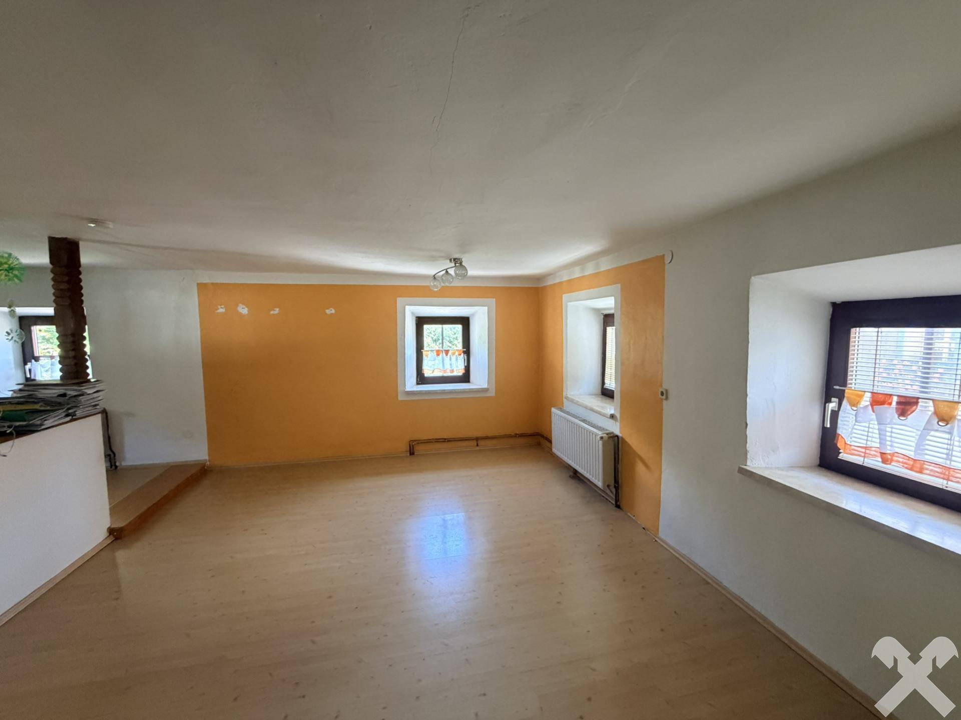 Geräumiges Wohnzimmer mit Laminatboden, farbigen Wänden und mehreren Fenstern.