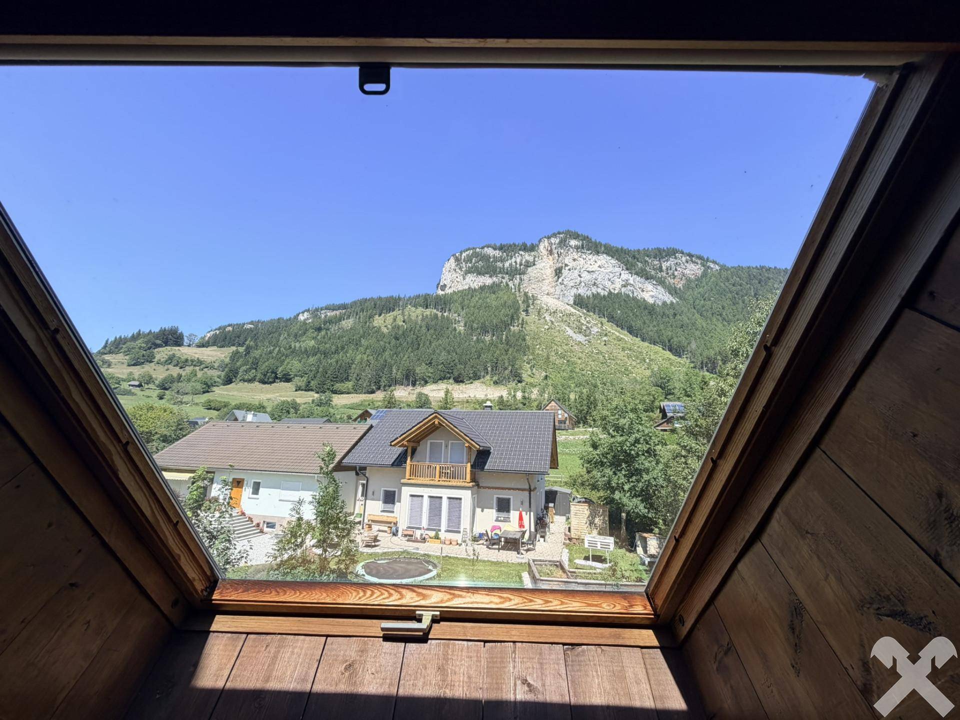 Panoramablick aus dem Dachfenster auf die umliegende Berglandschaft und Nachbarhäuser.