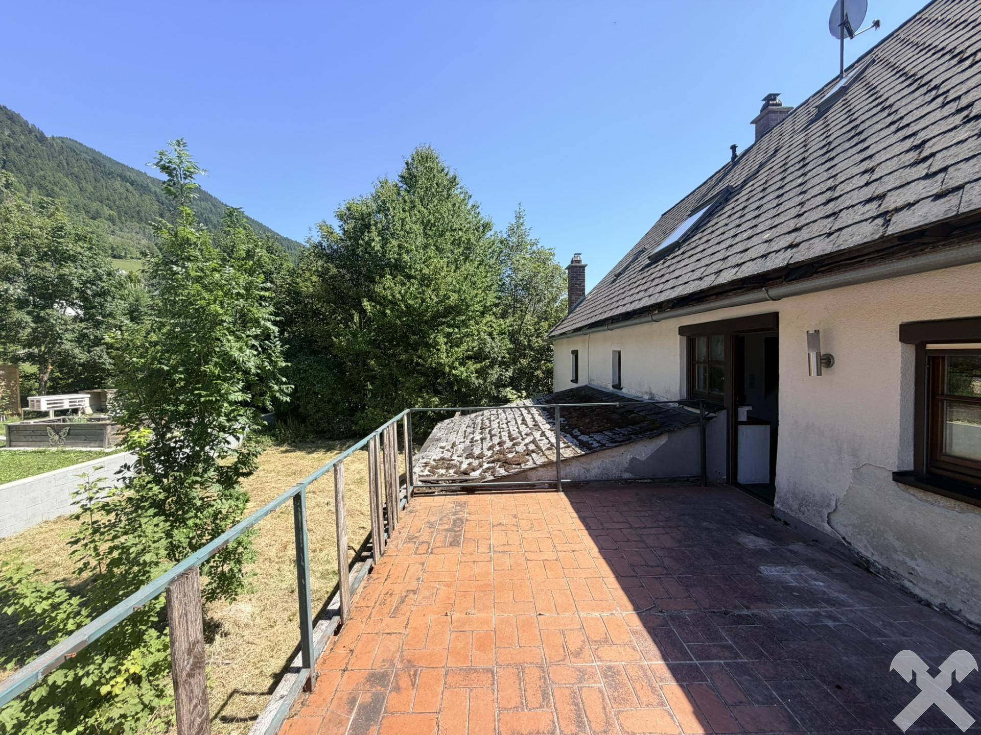 Geräumige Terrasse mit Ziegelboden und Blick auf das Haus sowie die grüne Umgebung.