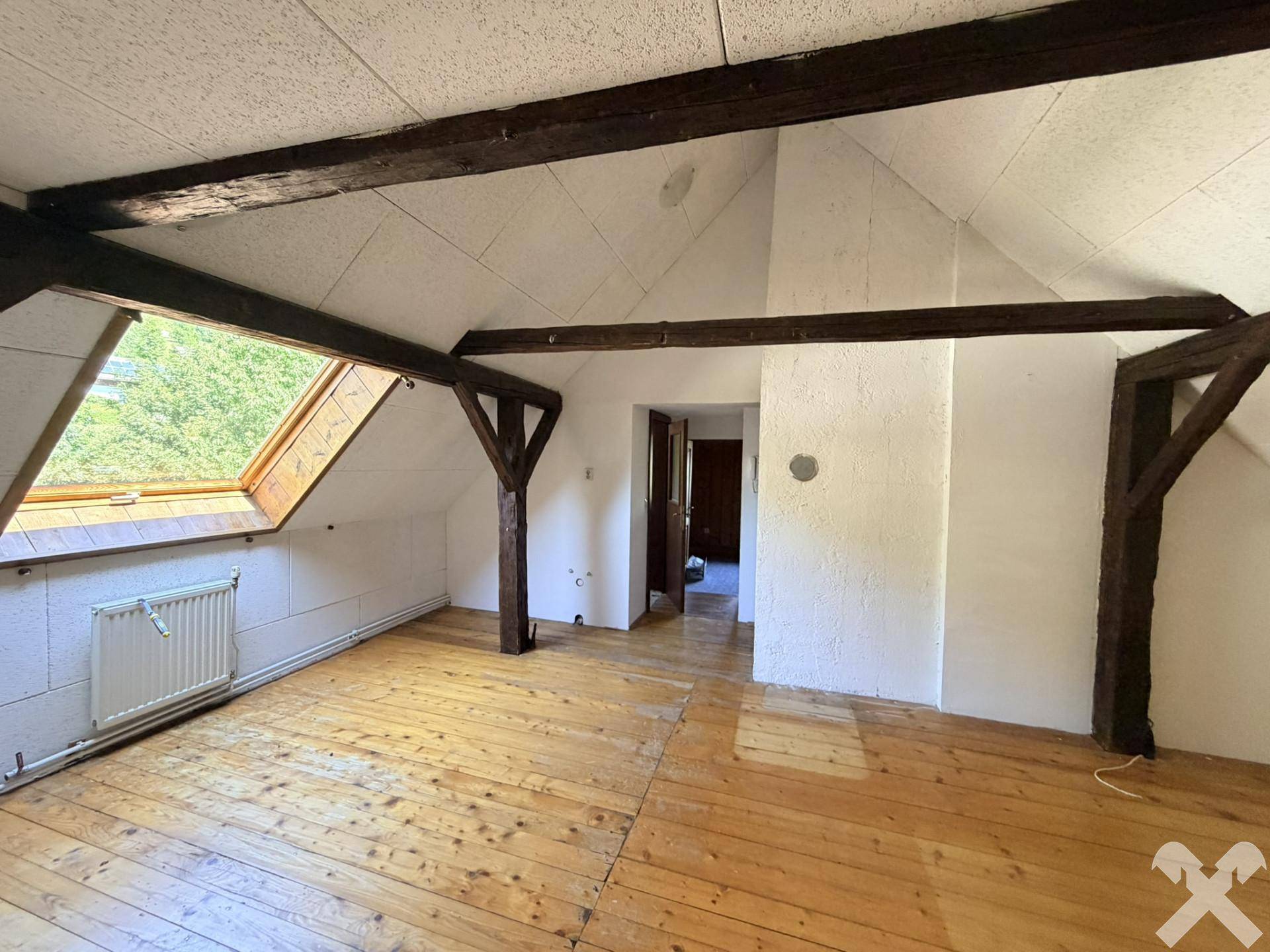 Geräumiges Dachzimmer mit sichtbaren Holzbalken, Dachschräge und Holzdielenboden.