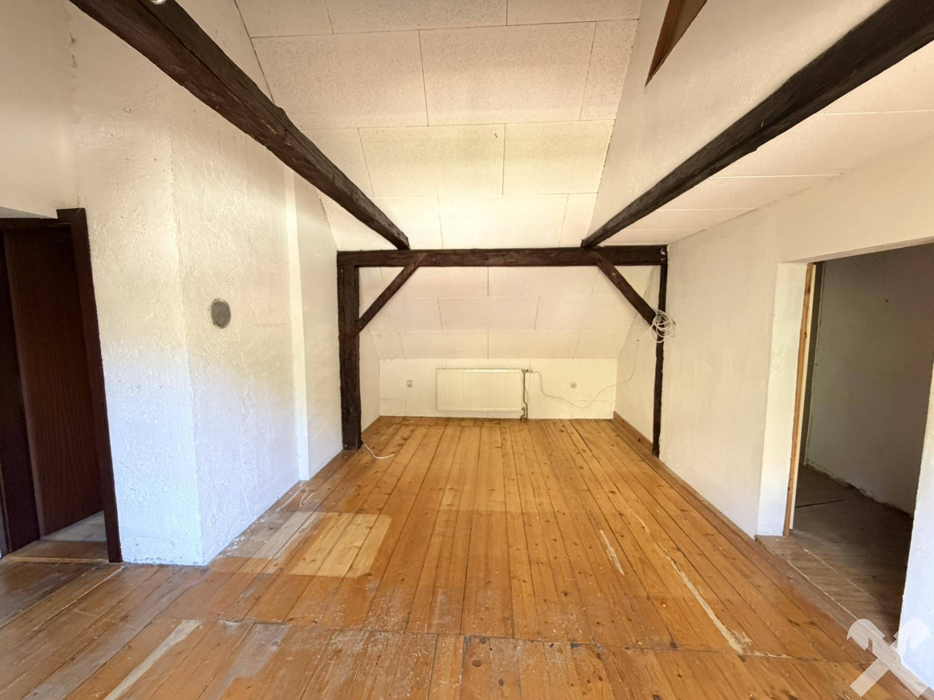 Helles Dachzimmer mit sichtbaren Holzbalken, Dachschräge und Holzdielenboden.
