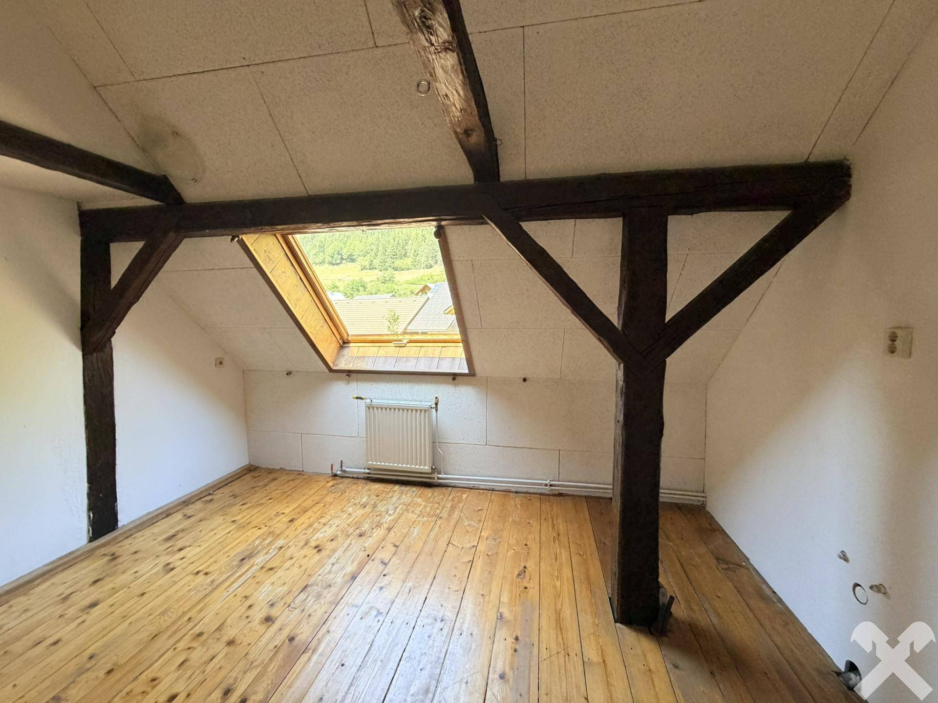 Dachzimmer mit Holzbalken, Dachschräge, Holzdielenboden und einem Dachfenster.