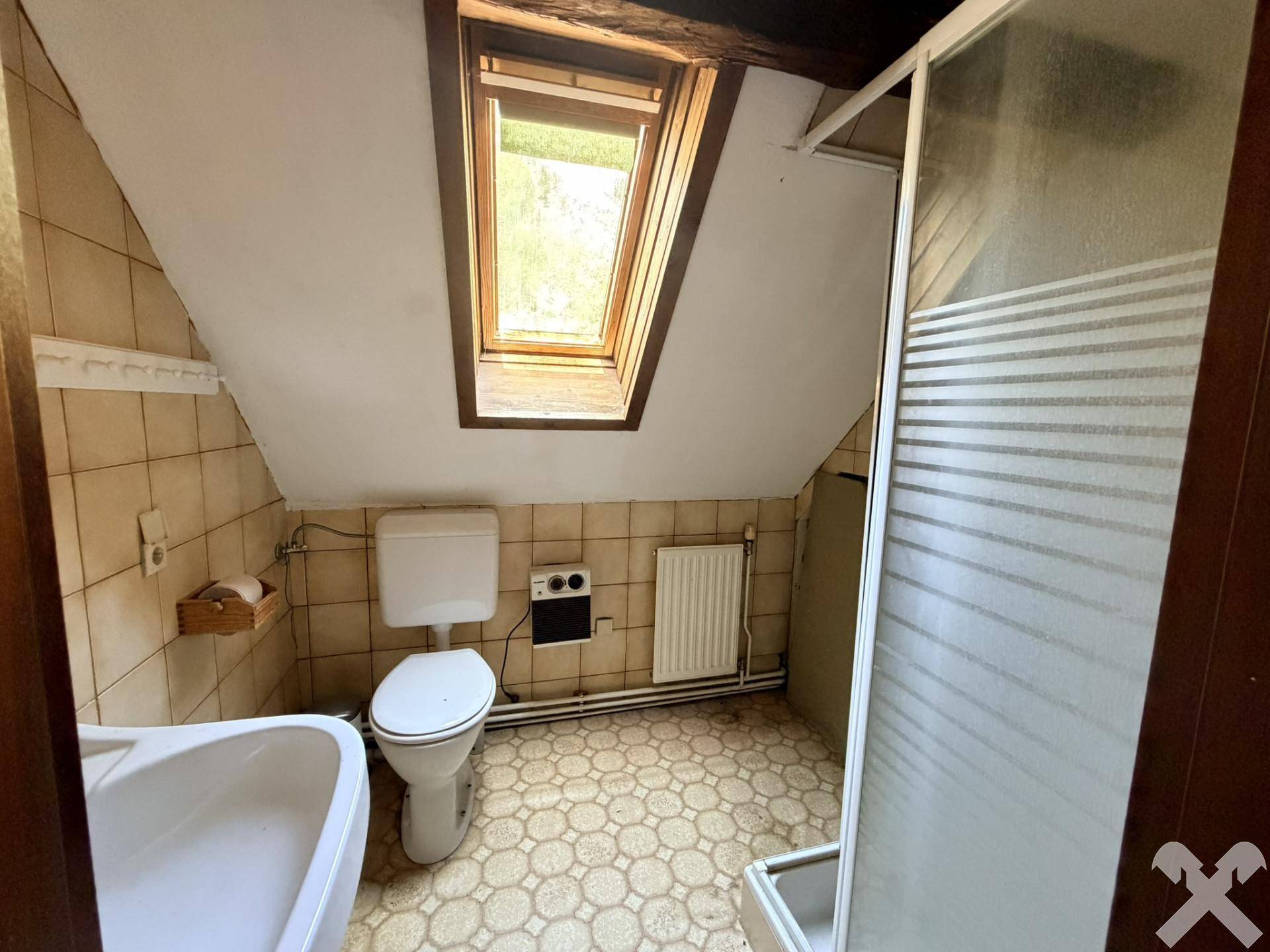 Badezimmer im Dachgeschoss mit Toilette, Waschbecken, Duschkabine und Dachfenster.