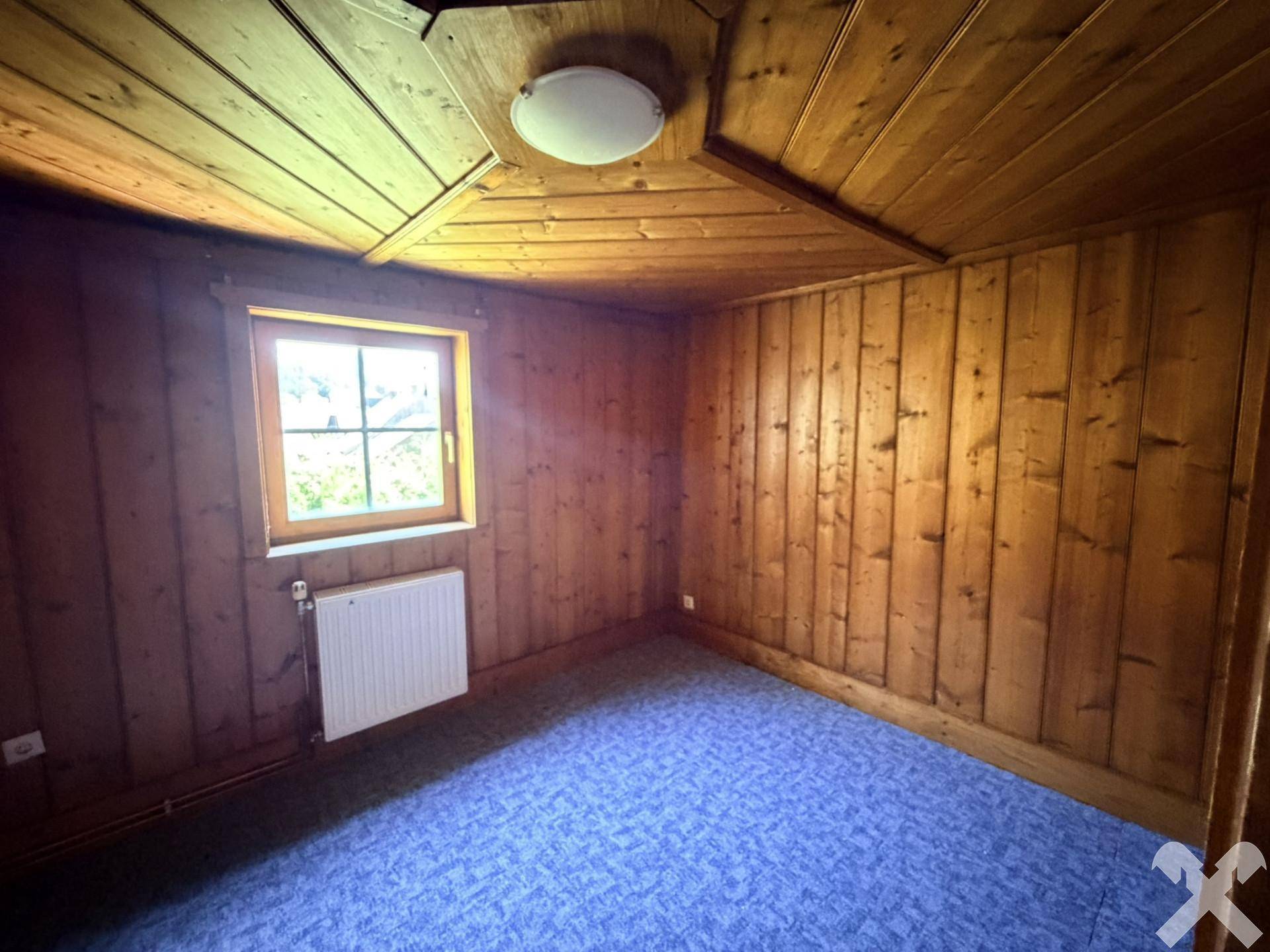 Gemütliches Zimmer mit holzvertäfelten Wänden und Decke sowie blauem Teppichboden.