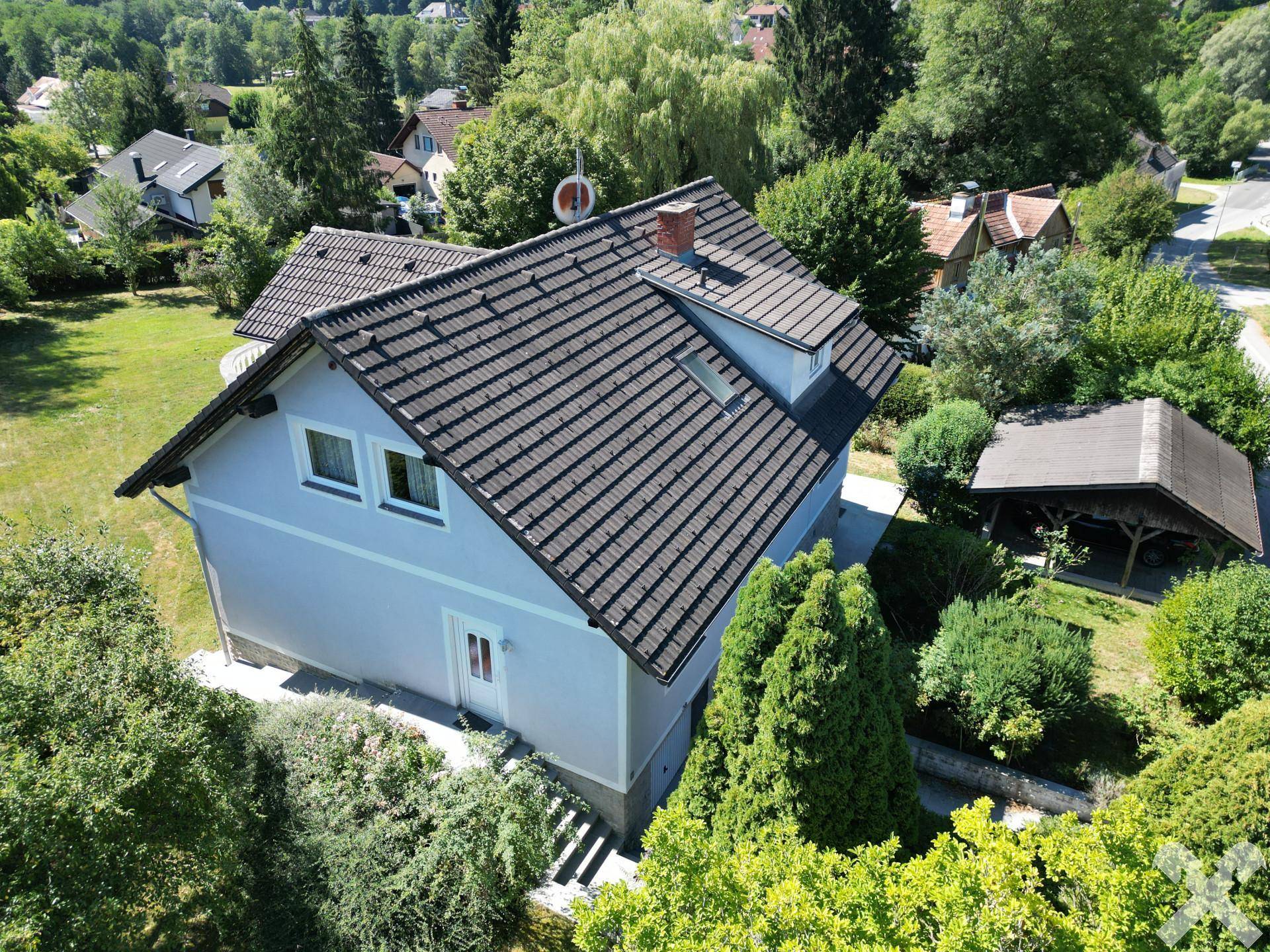 Seitenansicht des Hauses mit Satteldach, umgeben von viel Grün und Bäumen.