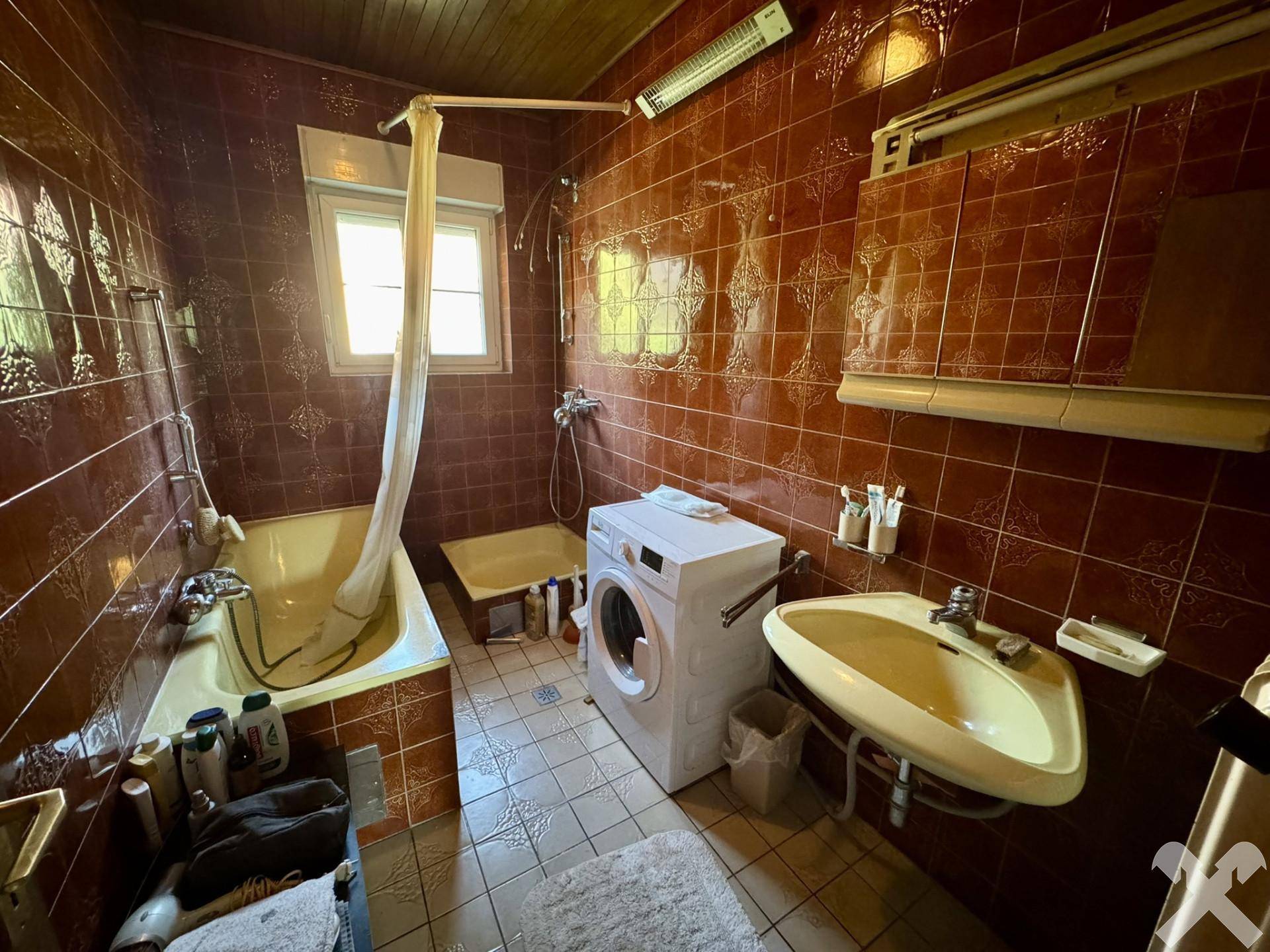 Badezimmer mit Badewanne, Waschmaschine und braunen Fliesen im Vintage-Stil.
