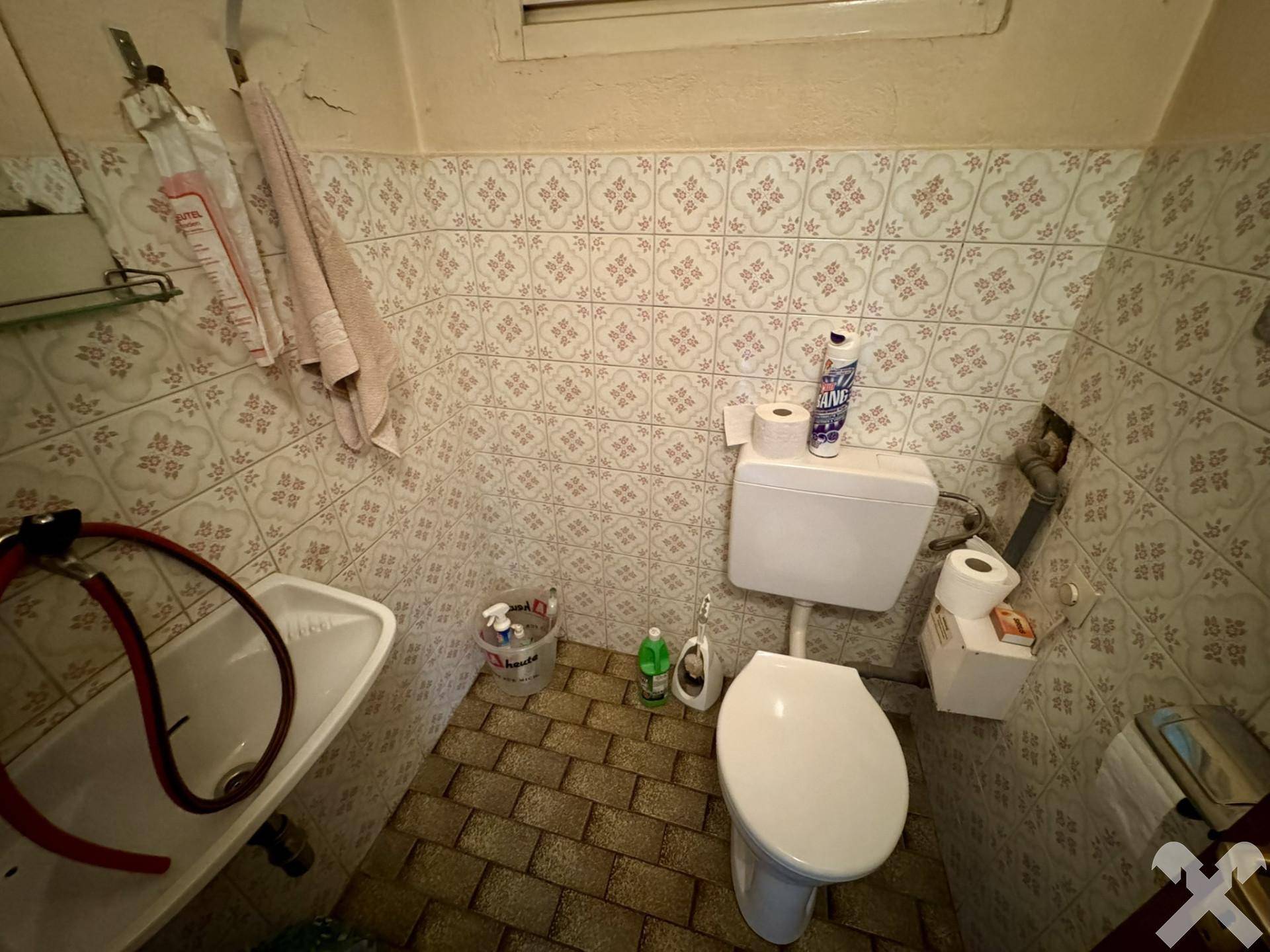 Separate Toilette mit Waschbecken und gemusterten Fliesen, funktional eingerichtet.
