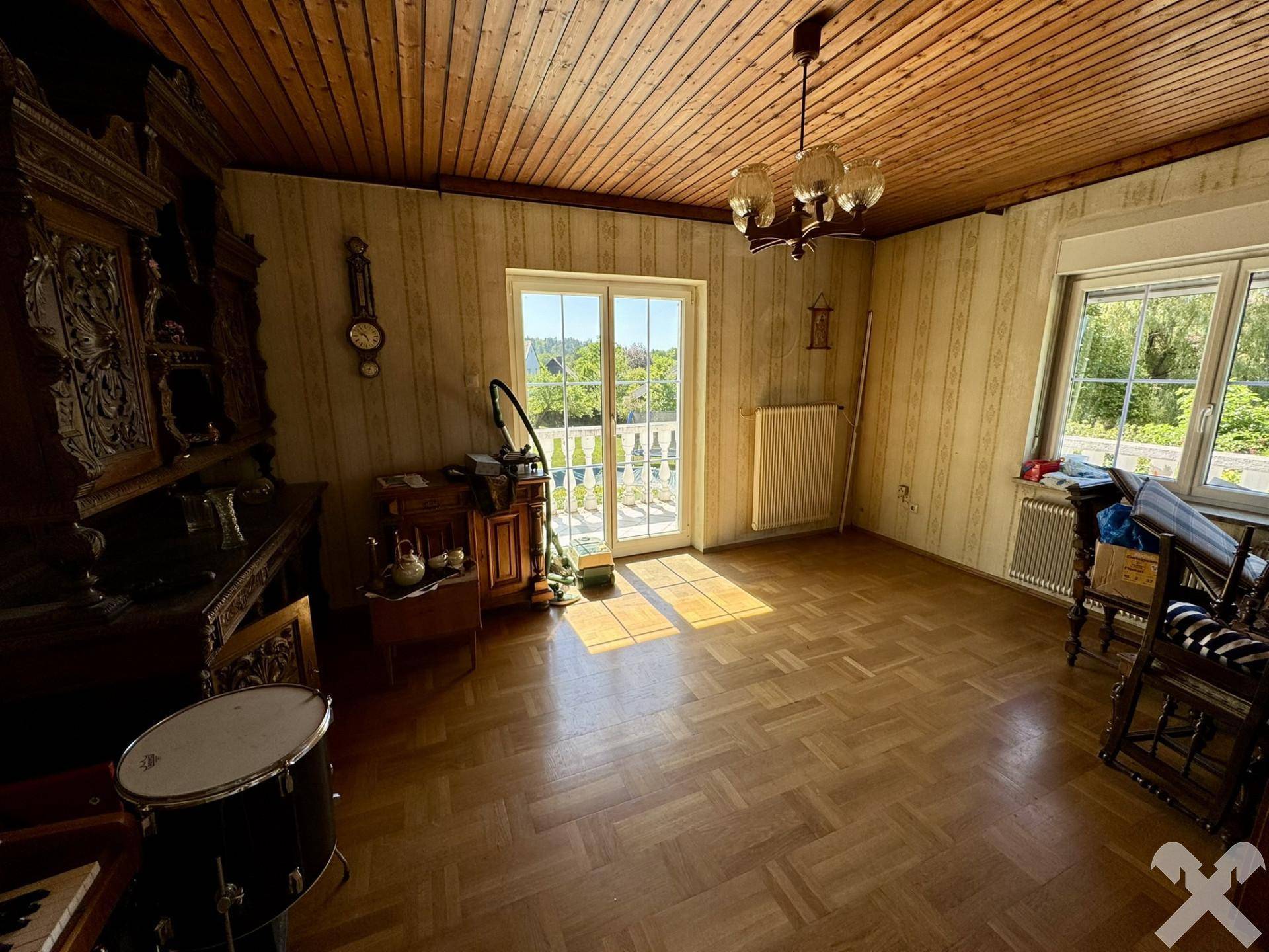 Gemütliches Wohnzimmer mit Parkettboden, Holzdecke und Zugang zum Balkon.