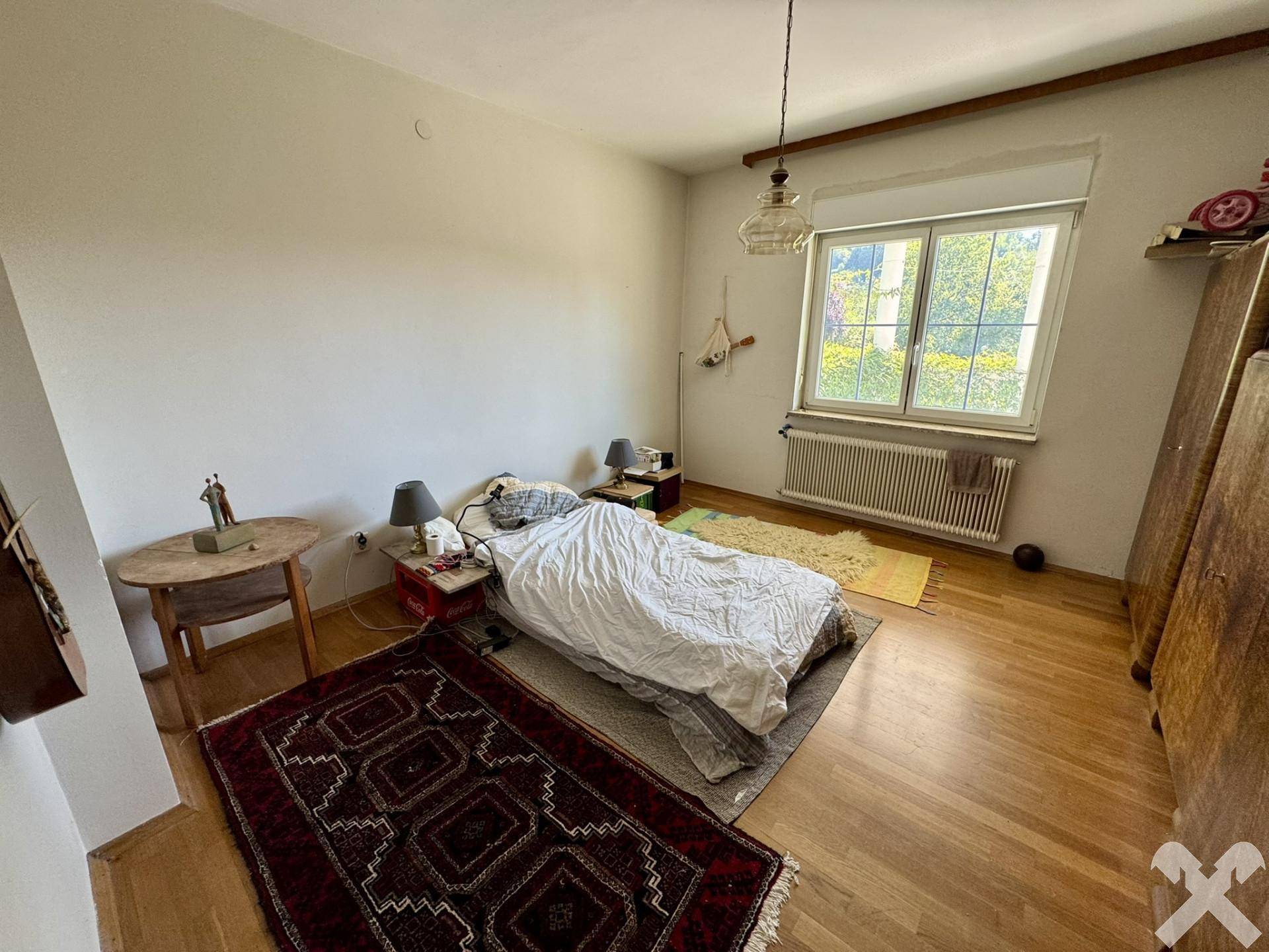 Schlafzimmer mit Parkettboden, großem Fenster und Blick ins Grüne.