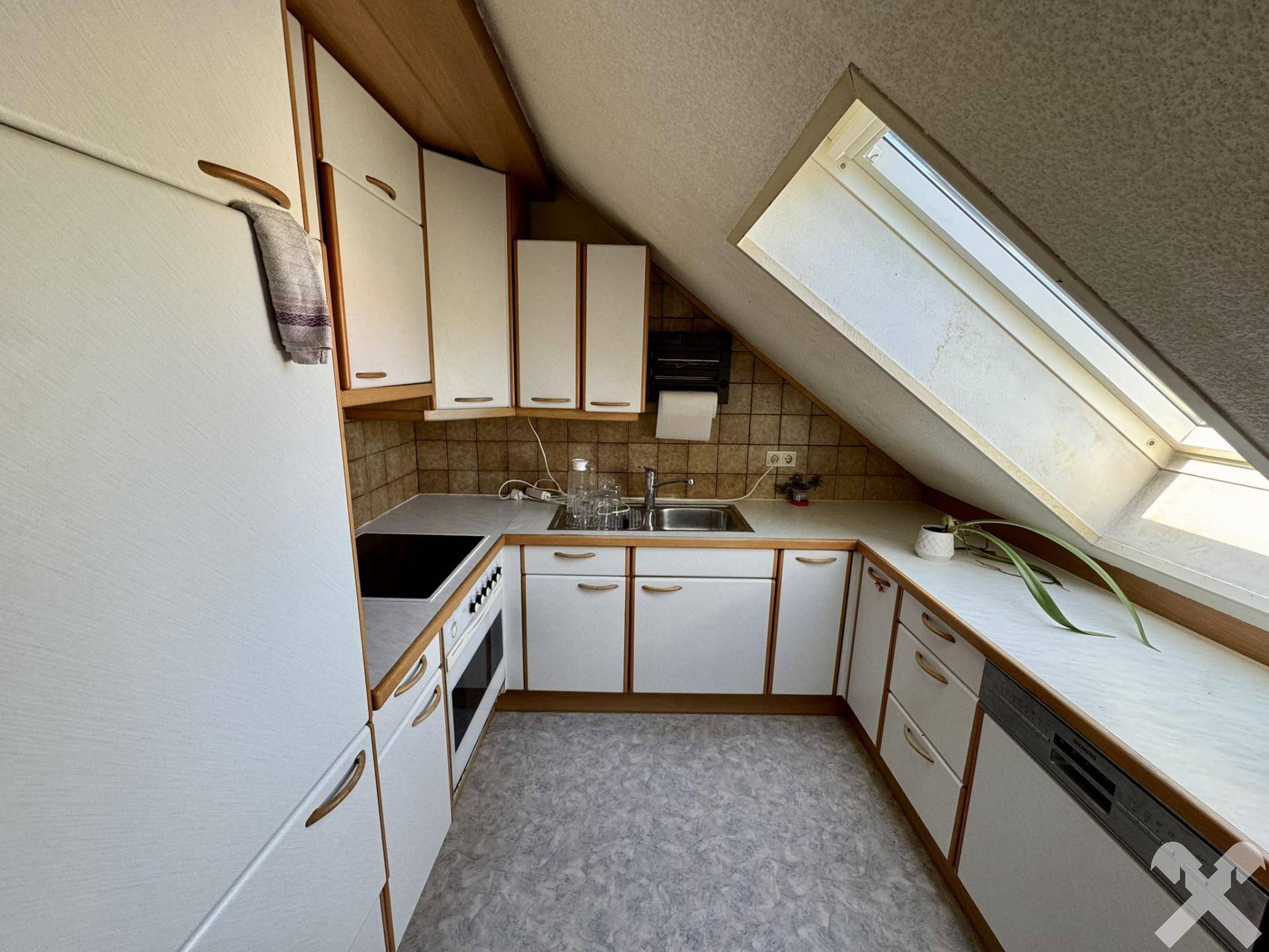 Dachgeschossküche mit Einbauküche, Dachfenster und schrägen Wänden.