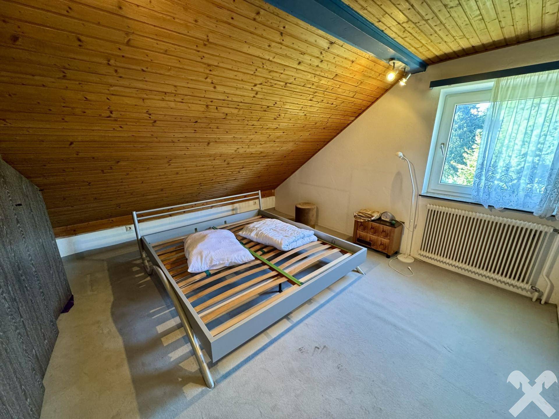 Schlafzimmer im Dachgeschoss mit Holzdecke, Holzbalken und großem Fenster.