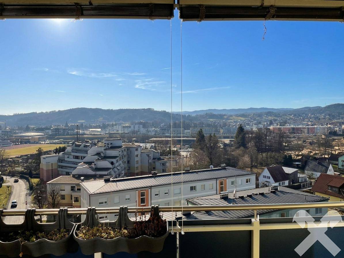 Sonniger Balkon mit weitem Blick über die Stadt und die umliegenden Hügel unter blauem Himmel.