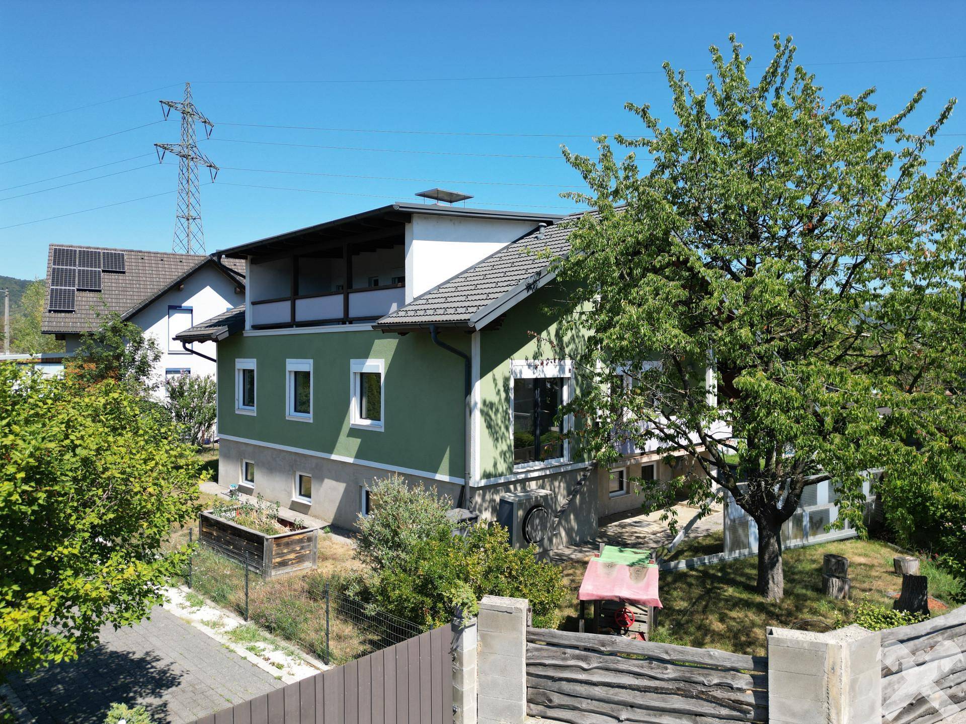 Seitenansicht des Hauses mit Balkon, grüner Fassade und umgebender Natur.