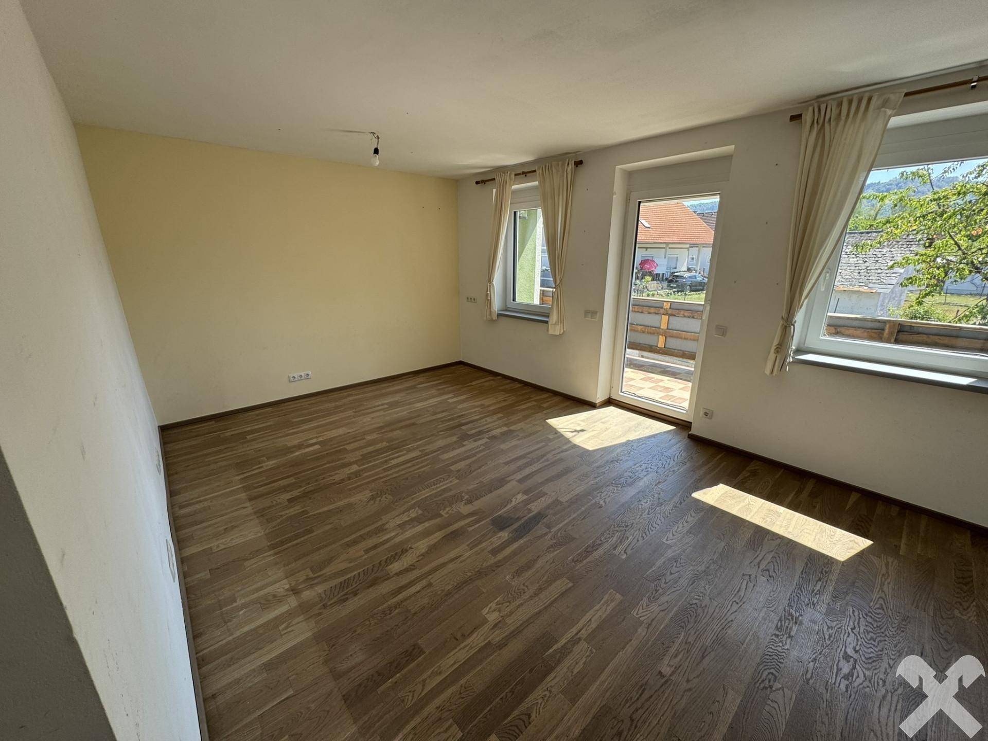 Helles, leeres Zimmer mit Holzboden und Zugang zu einem kleinen Balkon.