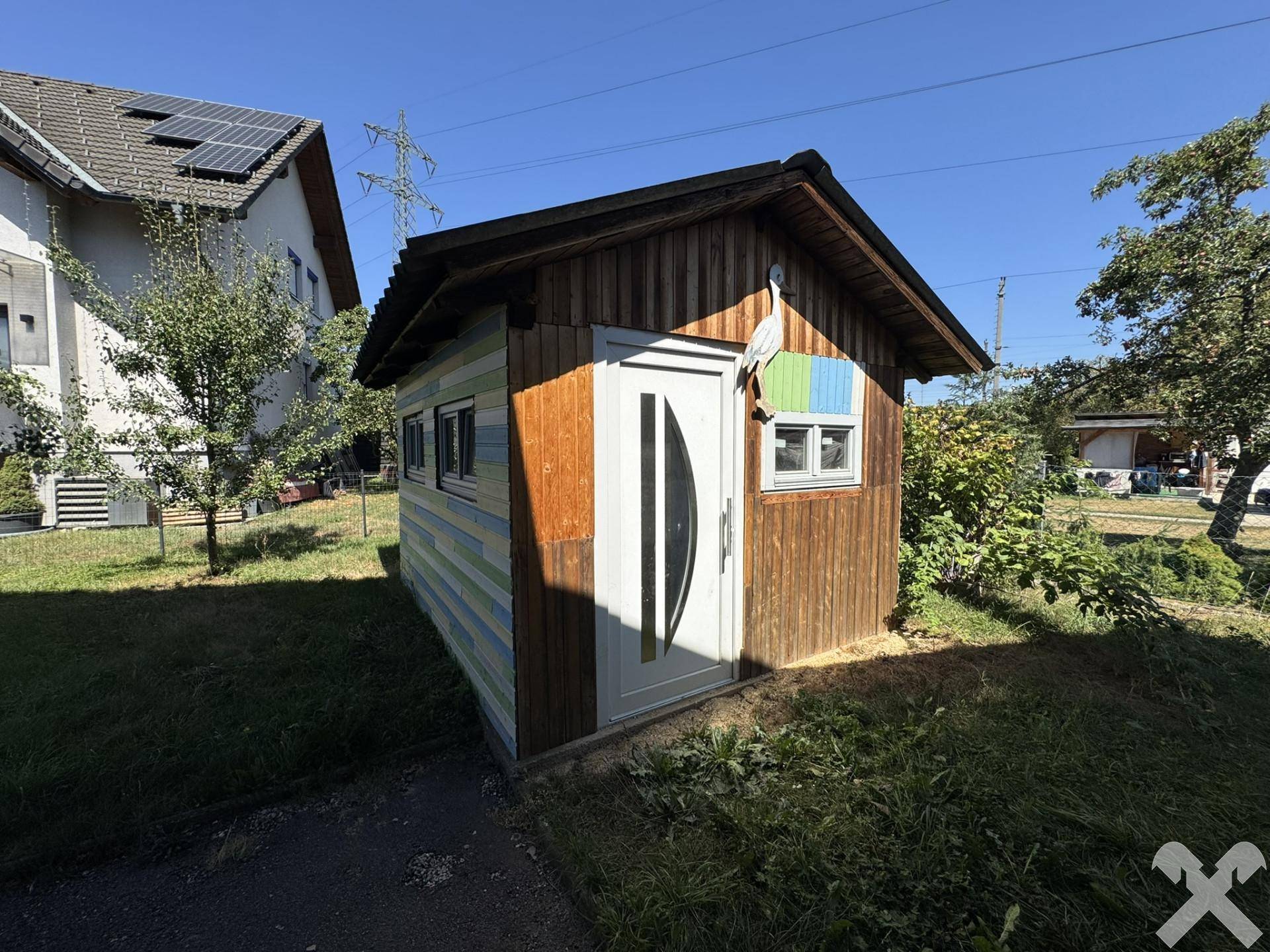 Kleines Gartenhaus aus Holz mit weißer Tür und bunten Akzenten im Grünen.