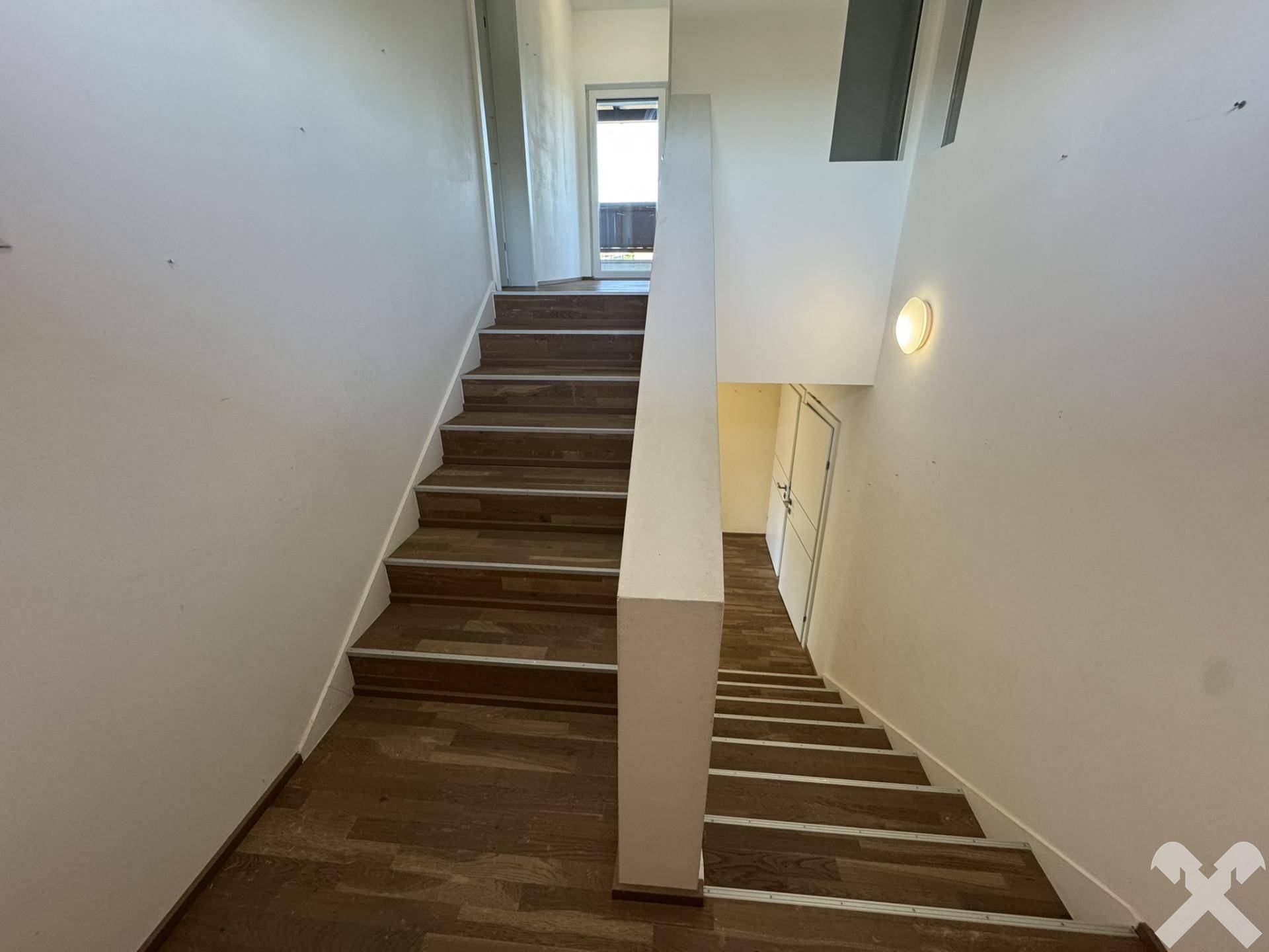 Treppenhaus mit Holzstufen und weiß gestrichenen Wänden, führt in obere Etagen.