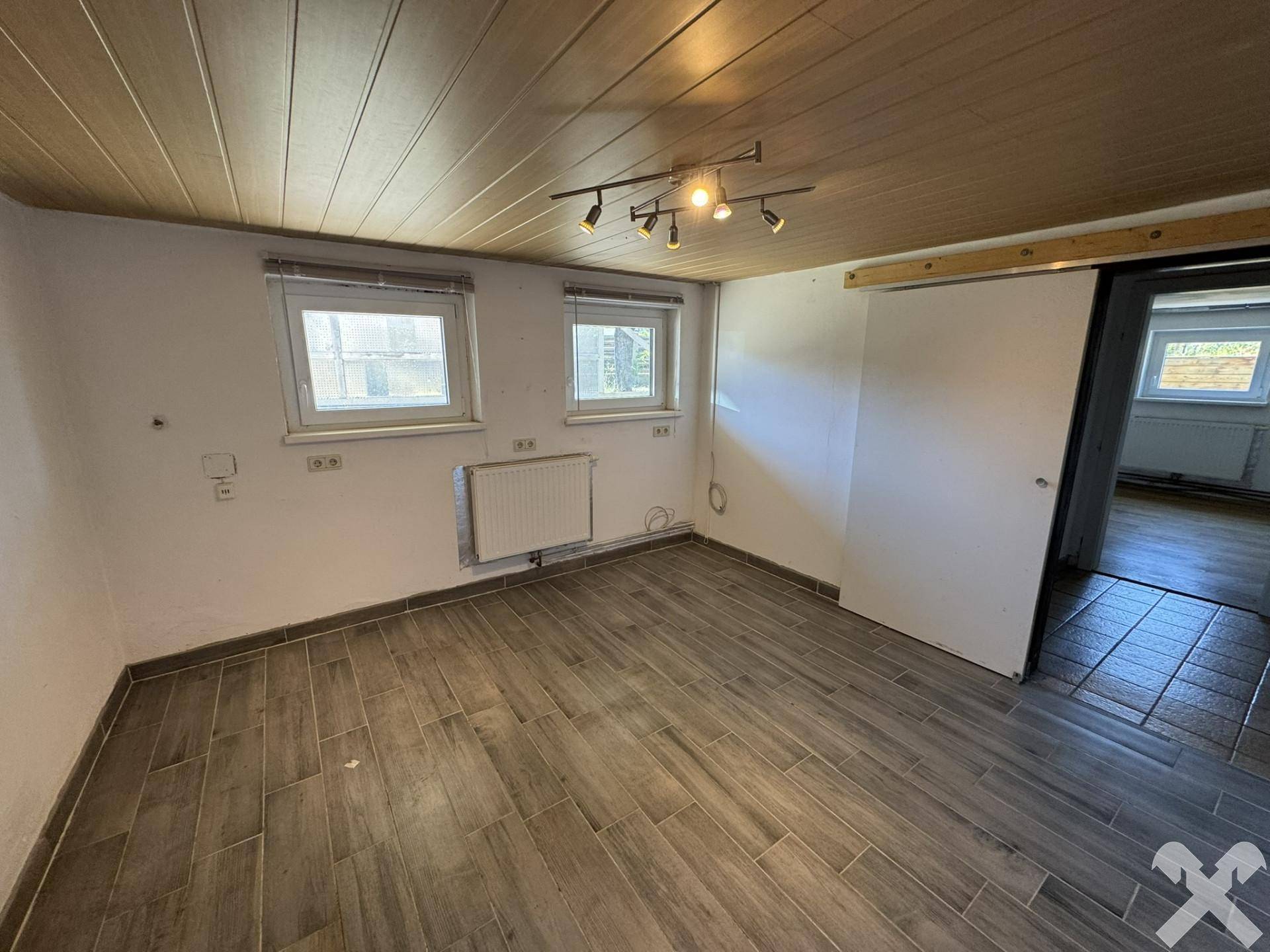 Kellerraum mit Fliesenboden und Holzdecke, ausgestattet mit Heizkörper.