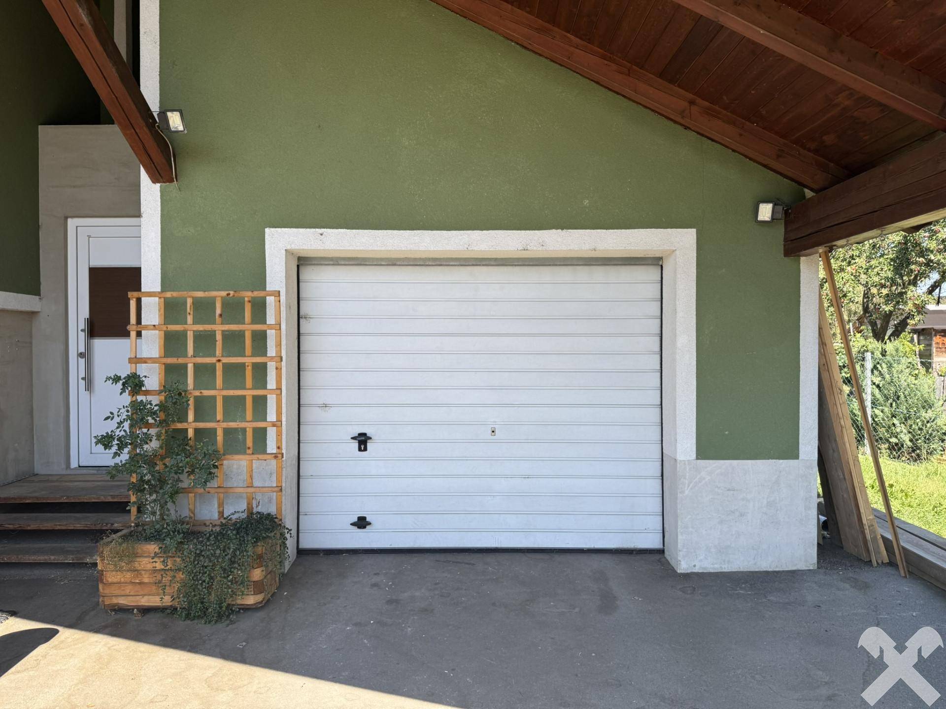 Einzelgarage mit weißem Garagentor und grün gestrichener Hausfassade.