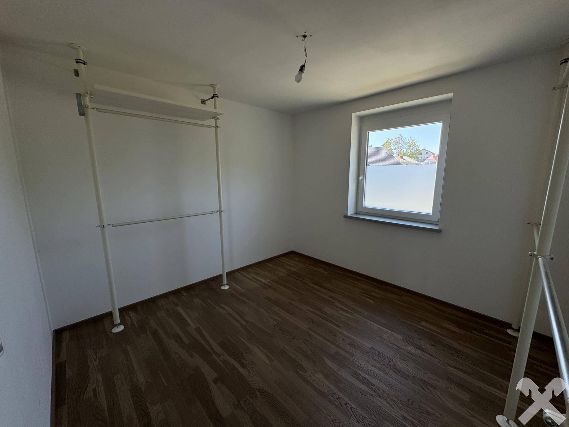 Leeres Zimmer mit Holzboden und einfacher Kleiderstange, ideal als Schlafzimmer.