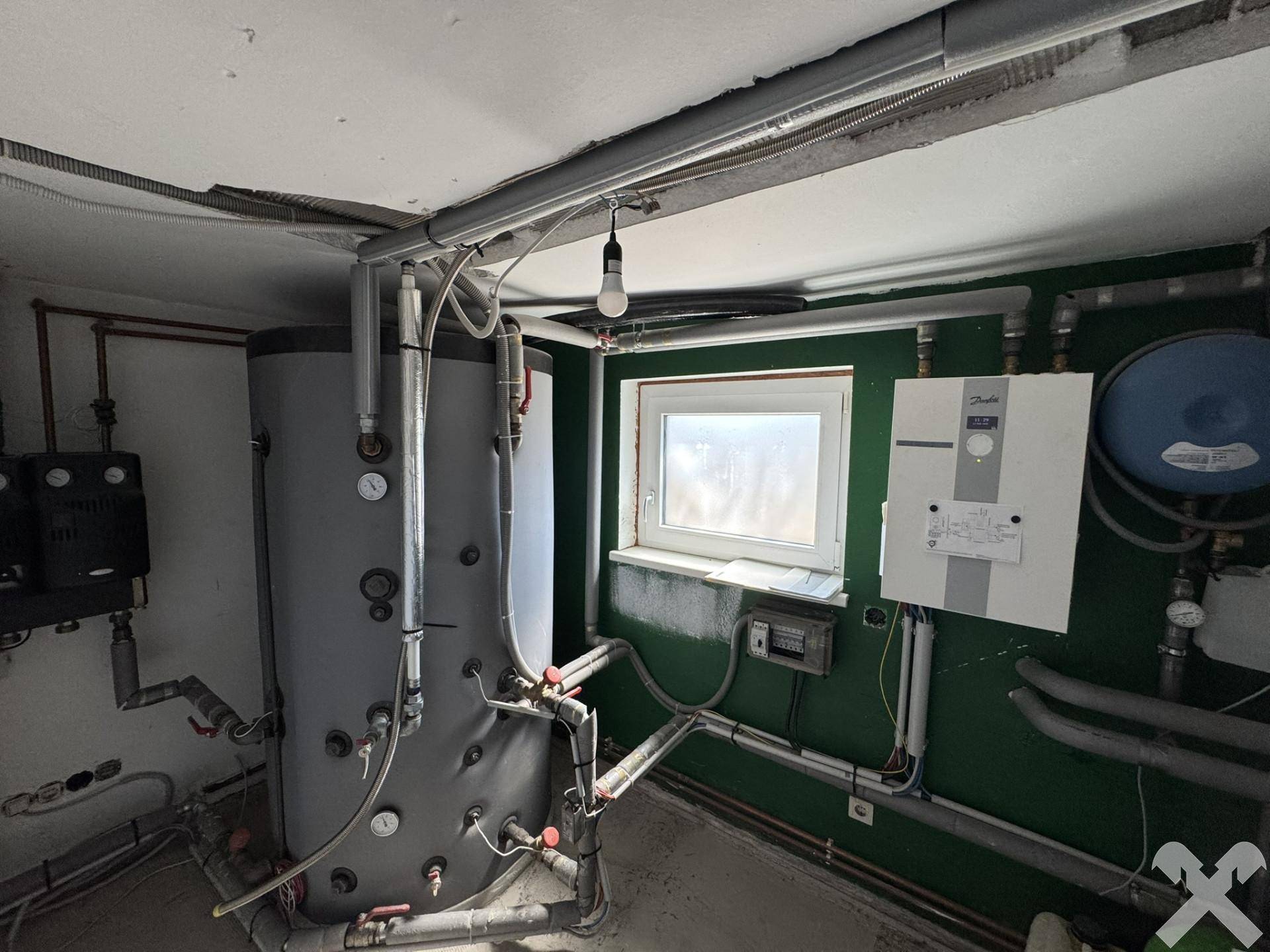 Heizungsraum mit Warmwasserspeicher und Rohrleitungen, funktional eingerichtet.