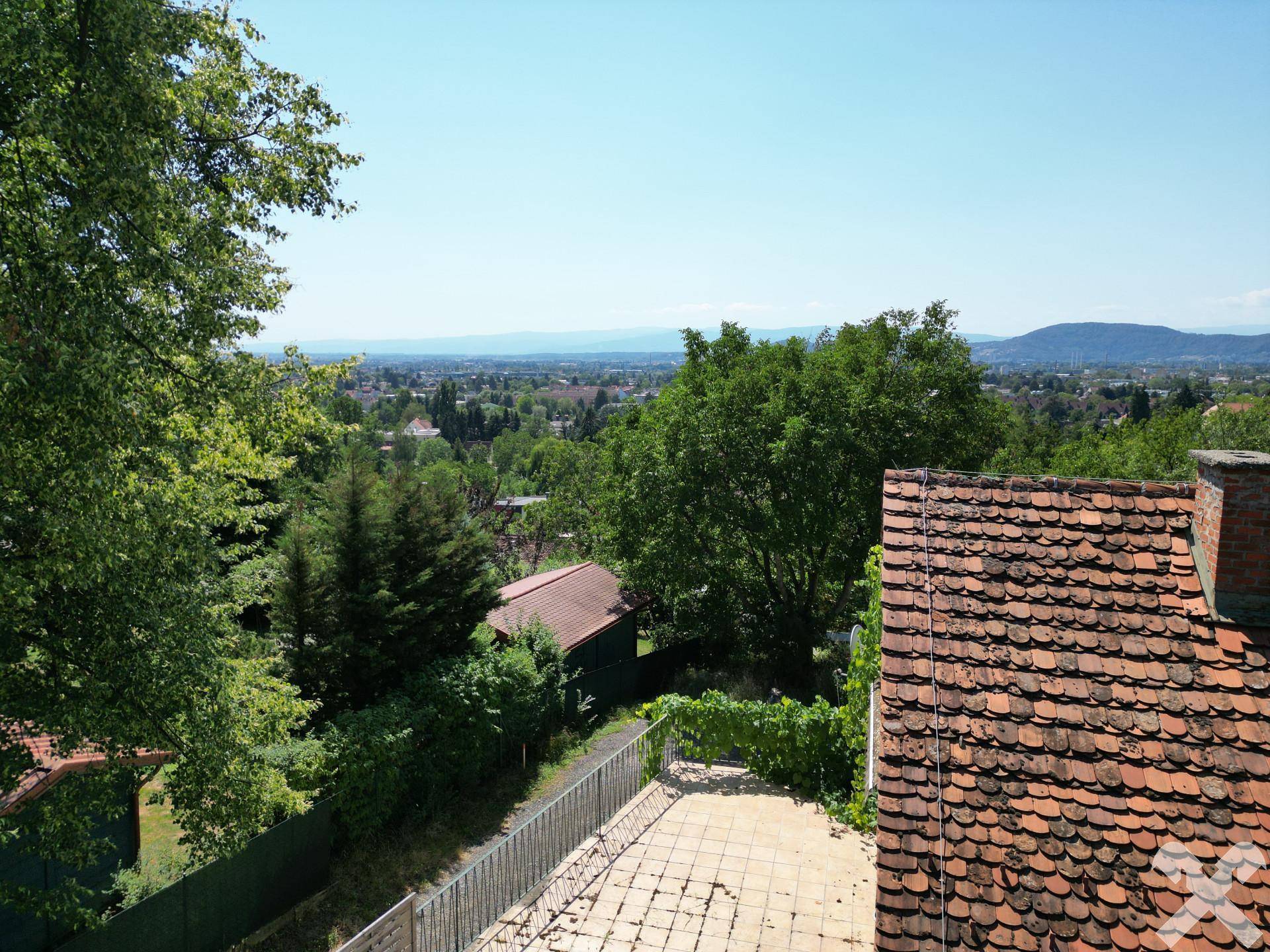Aussicht von der Terrasse auf die Stadt und die weite Landschaft mit Bergen am Horizont.