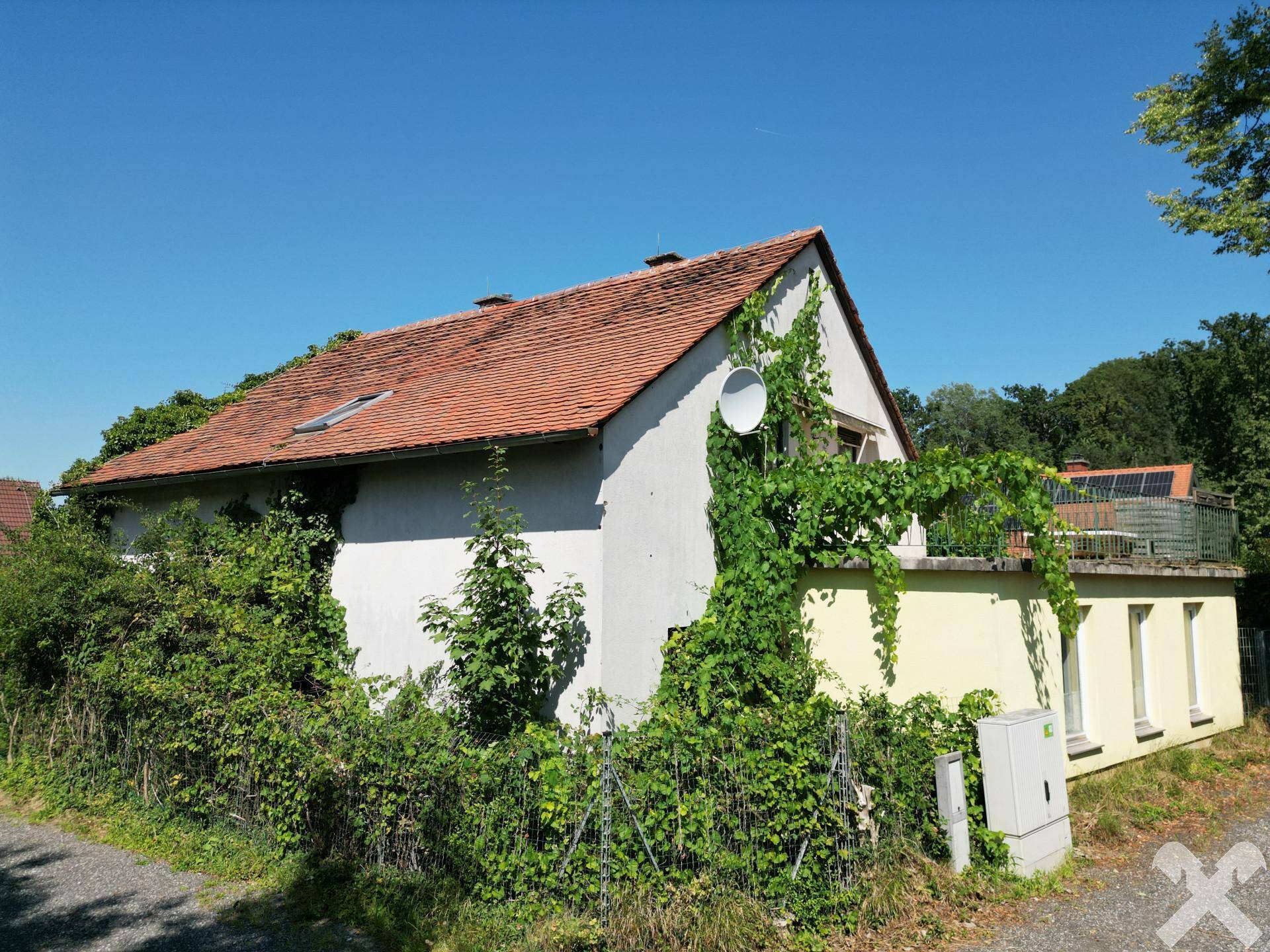 Seitenansicht des Hauses mit bewachsenen Wänden und einem kleinen Balkon unter blauem Himmel.