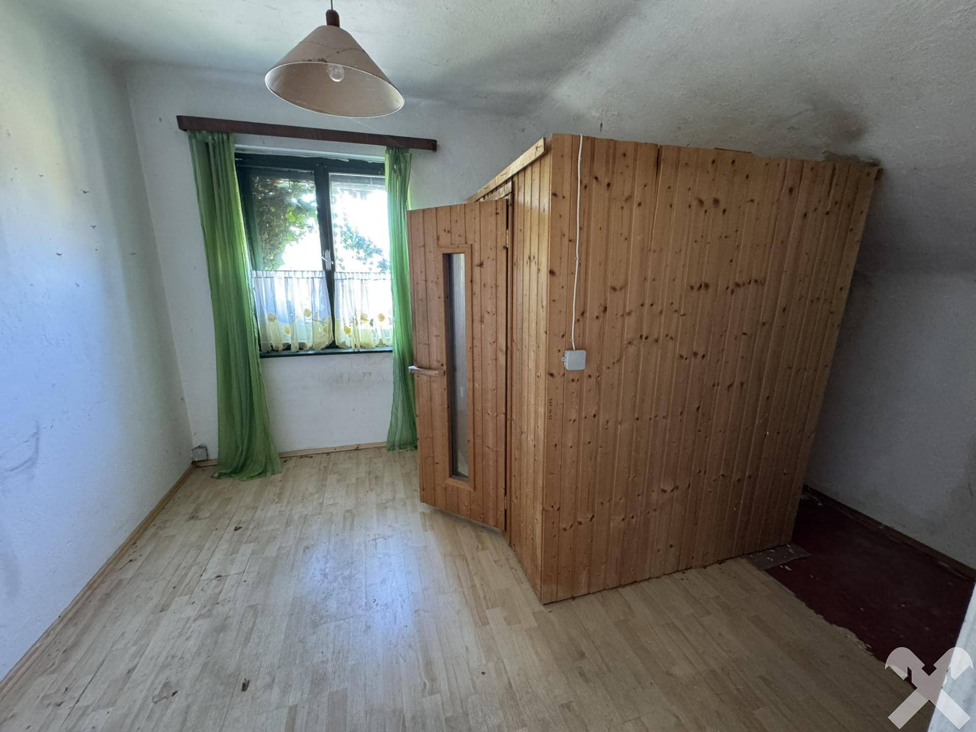 Raum mit einer Holzkabine, die eine Sauna beherbergt, und einem Fenster mit grüner Aussicht.