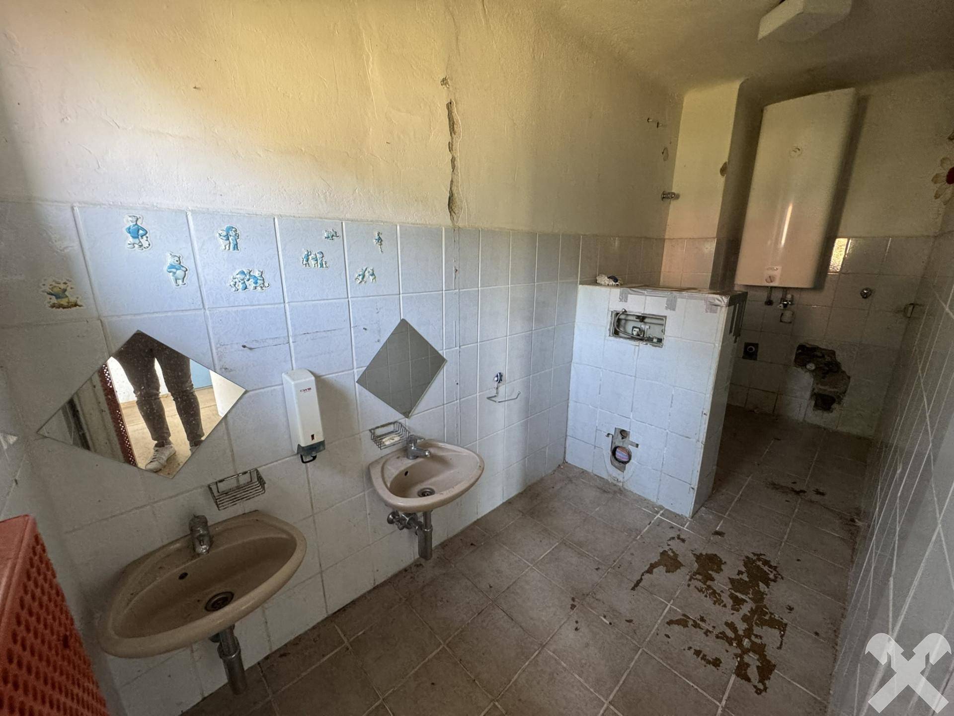 Badezimmer mit zwei Waschbecken, gefliesten Wänden und einem Warmwasserbereiter, renovierungsbedürftig.