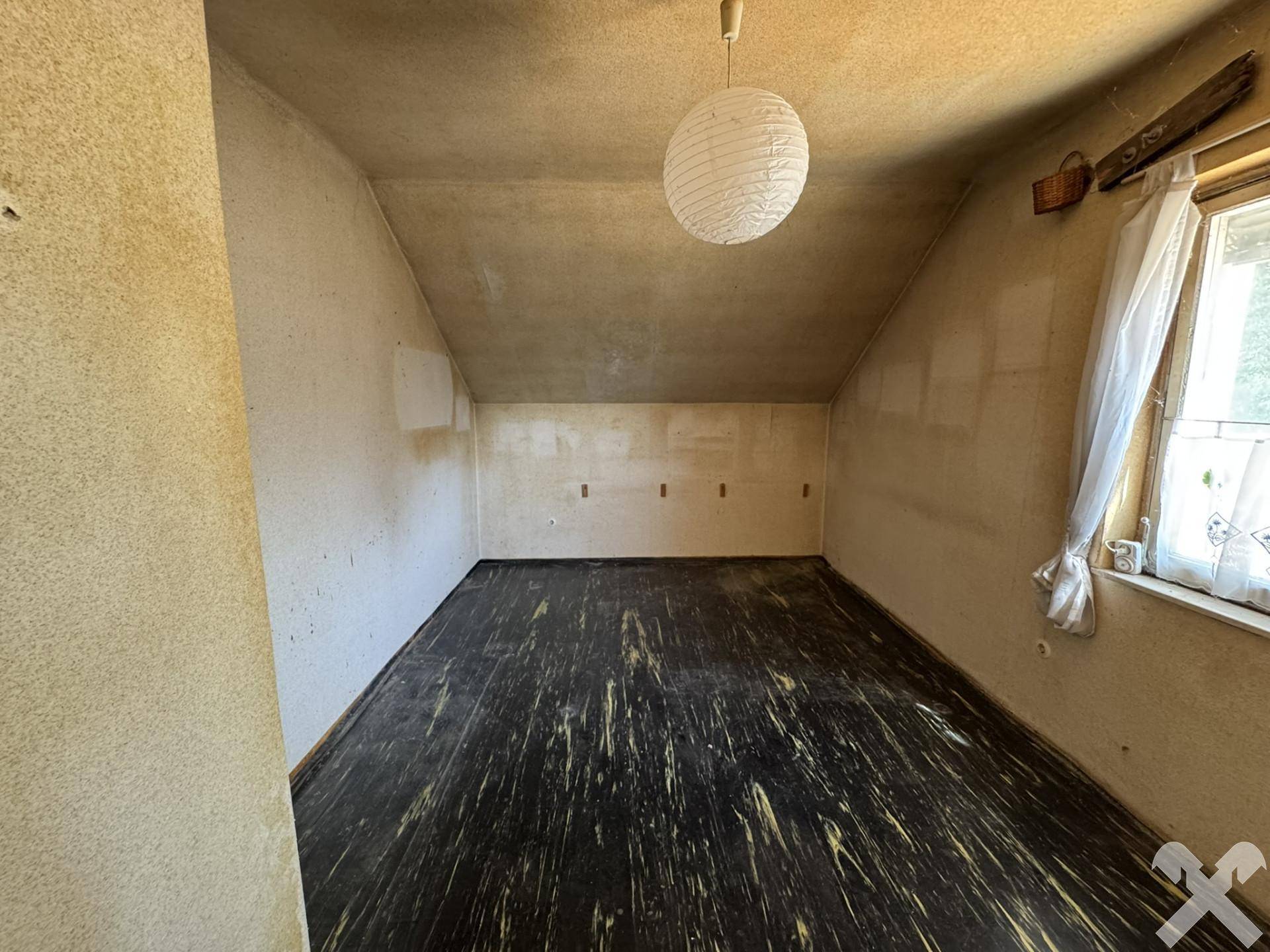 Kleines Dachzimmer mit dunklem Holzboden und einem Fenster, das natürliches Licht hereinlässt.