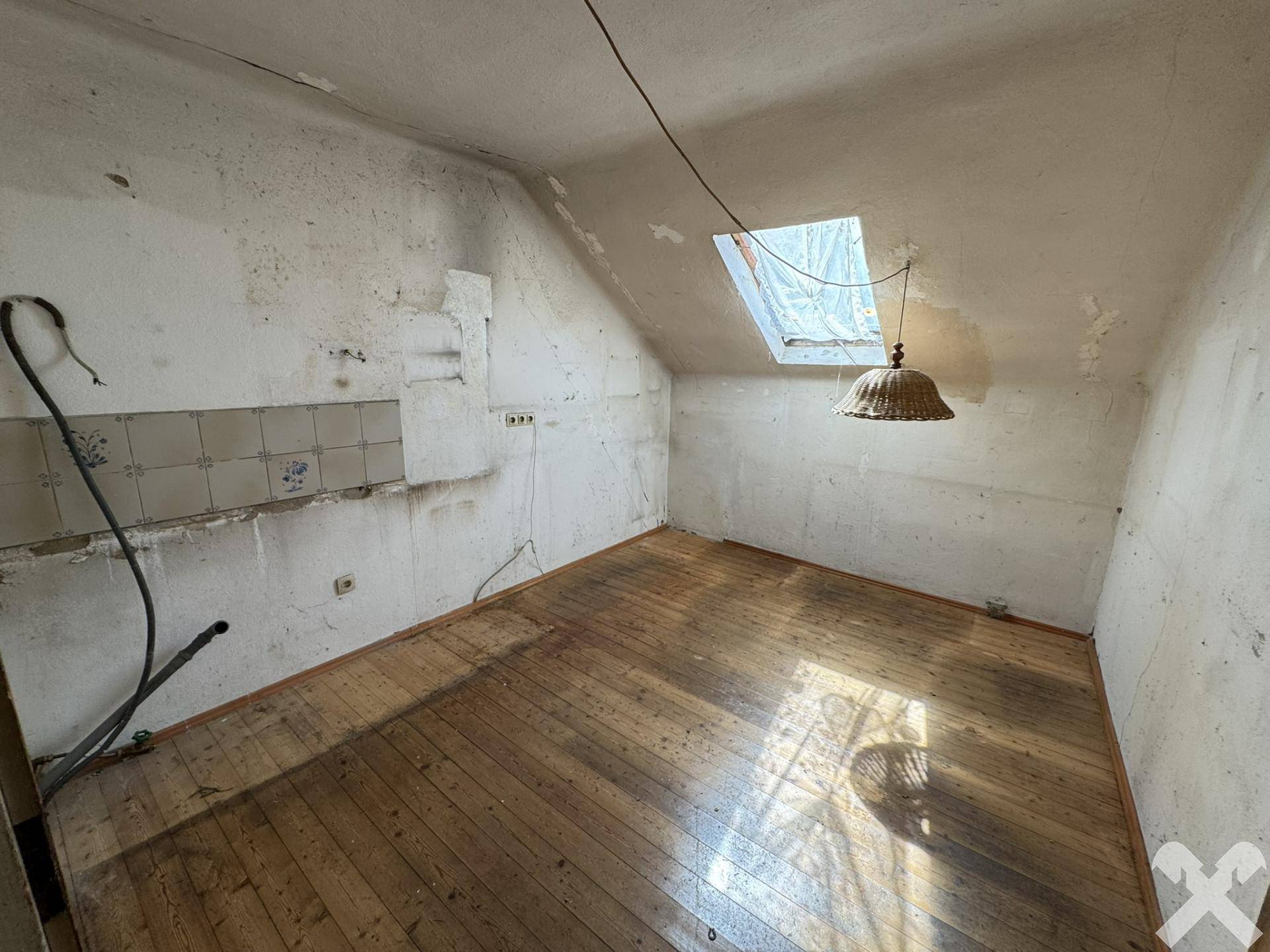 Dachzimmer mit Holzboden, Dachfenster und renovierungsbedürftigen Wänden, bietet viel Potenzial.