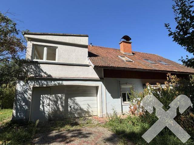 Vorderansicht des Hauses mit integrierter Garage und rotem Ziegeldach, umgeben von Sträuchern.