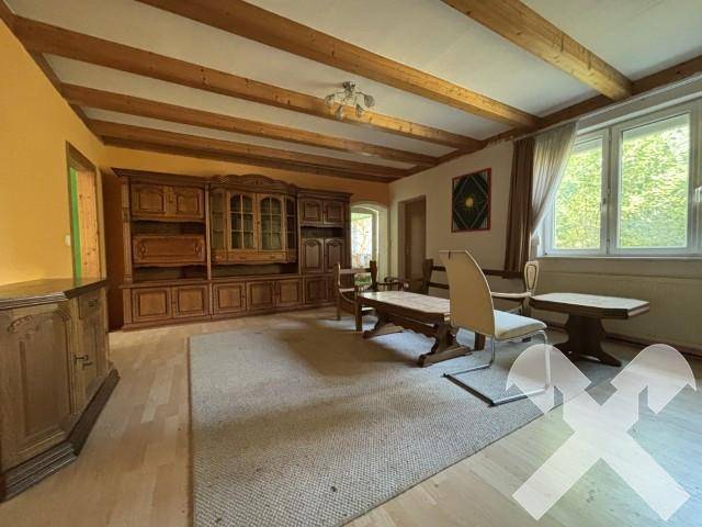 Geräumiges Wohnzimmer mit sichtbaren Holzdeckenbalken, traditionellen Möbeln und Parkettboden.