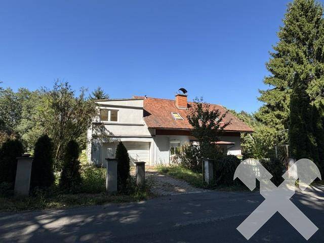 Vorderansicht des Hauses mit Garage und rotem Ziegeldach, umgeben von Bäumen und Sträuchern.