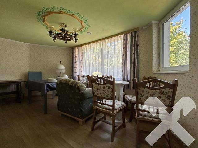 Esszimmer mit gemusterter Tapete, traditionellen Holzmöbeln und einem großen Fenster mit Vorhängen.