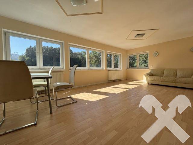 Lichtdurchfluteter Wohnbereich mit Holzfußboden, großen Fenstern und einem beigen Sofa.