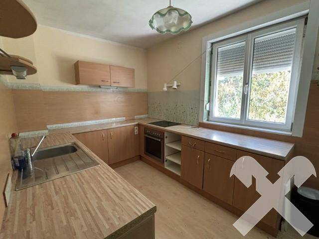 Funktionale Küche mit Holzschränken, Arbeitsplatten in Holzoptik und einem Fenster mit Rollladen.
