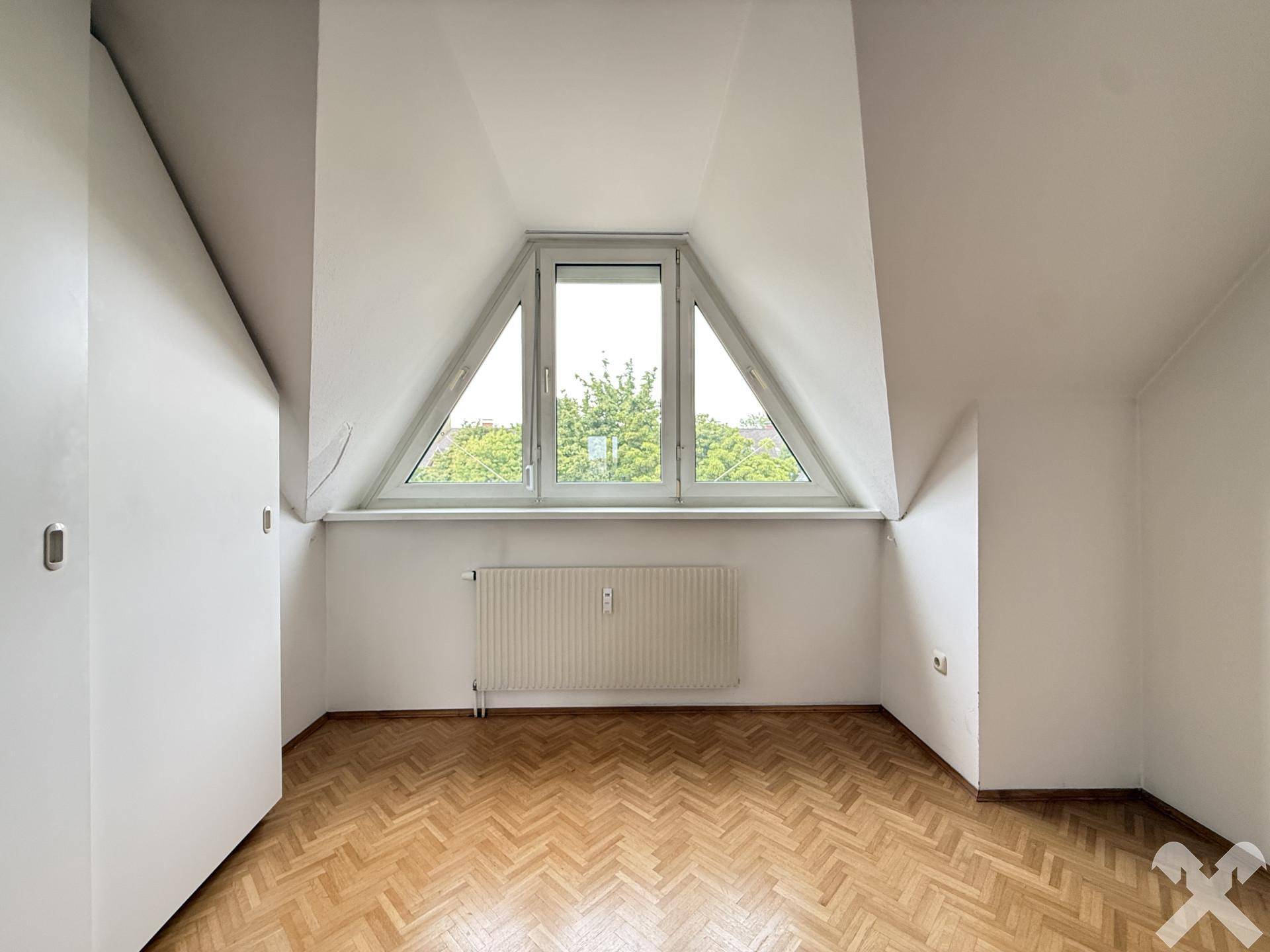 Gemütliches Zimmer im Dachgeschoss mit Parkettboden, schrägen Wänden und Blick ins Grüne.