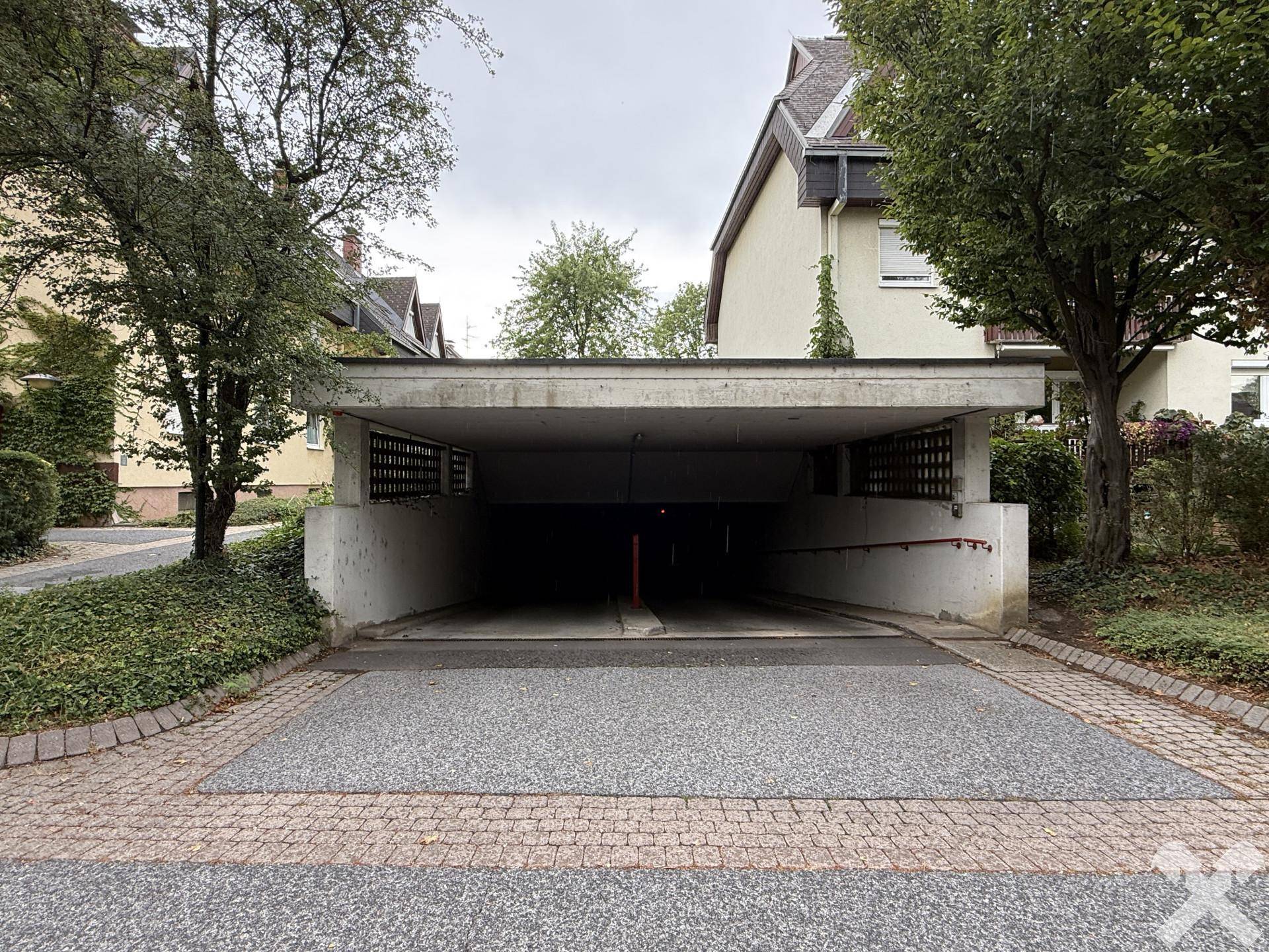 Eingang zu einer Tiefgarage mit Betonkonstruktion und Zufahrt, umgeben von Bäumen.